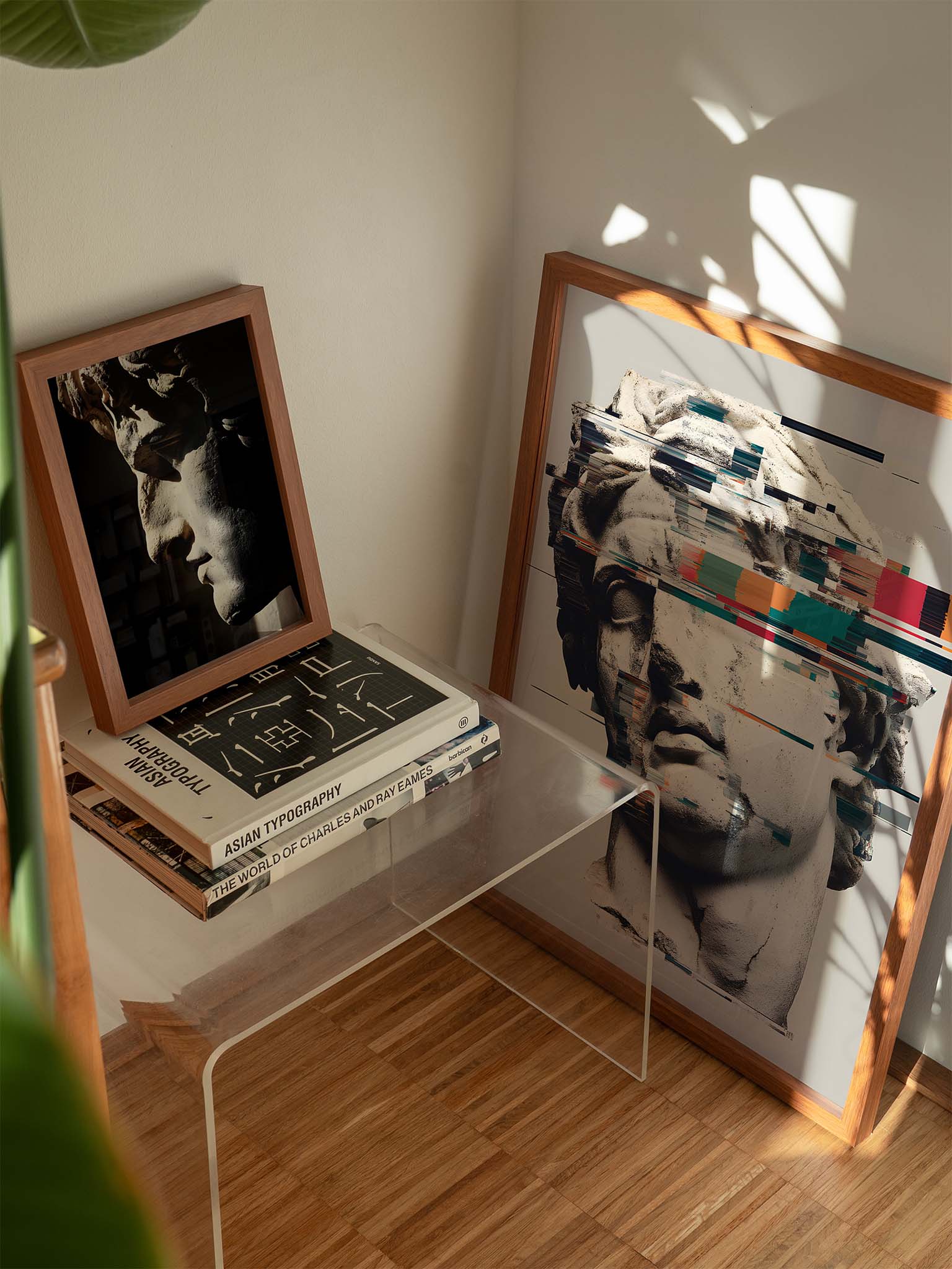 Gerahmtes Kunstbild einer klassischen Skulptur mit modernem Glitch-Effekt, platziert auf einem transparenten Beistelltisch neben Büchern und einem weiteren Skulpturenporträt im warmen Sonnenlicht.