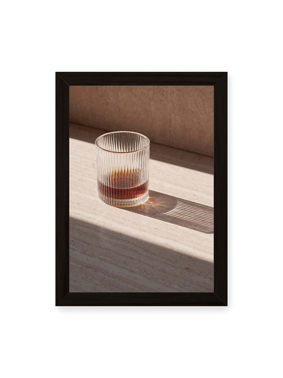 21x30 cm, schwarzer Rahmen – Geripptes Glas mit bernsteinfarbener Flüssigkeit auf heller Steinfläche im direkten Licht.