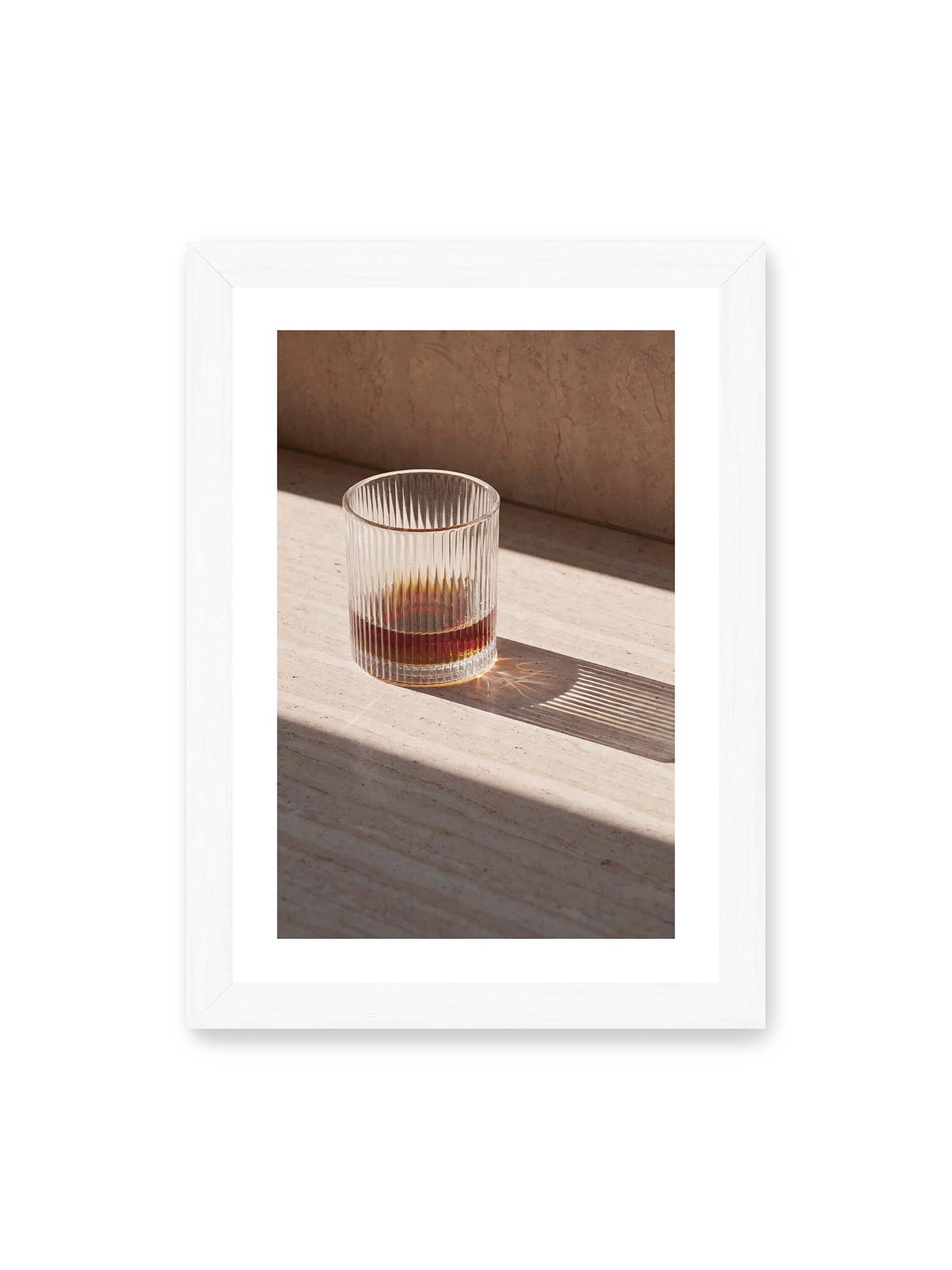 21x30 cm, weißer Galerie-Rand, weißer Rahmen – Geripptes Glas mit bernsteinfarbener Flüssigkeit auf heller Steinfläche im direkten Licht.