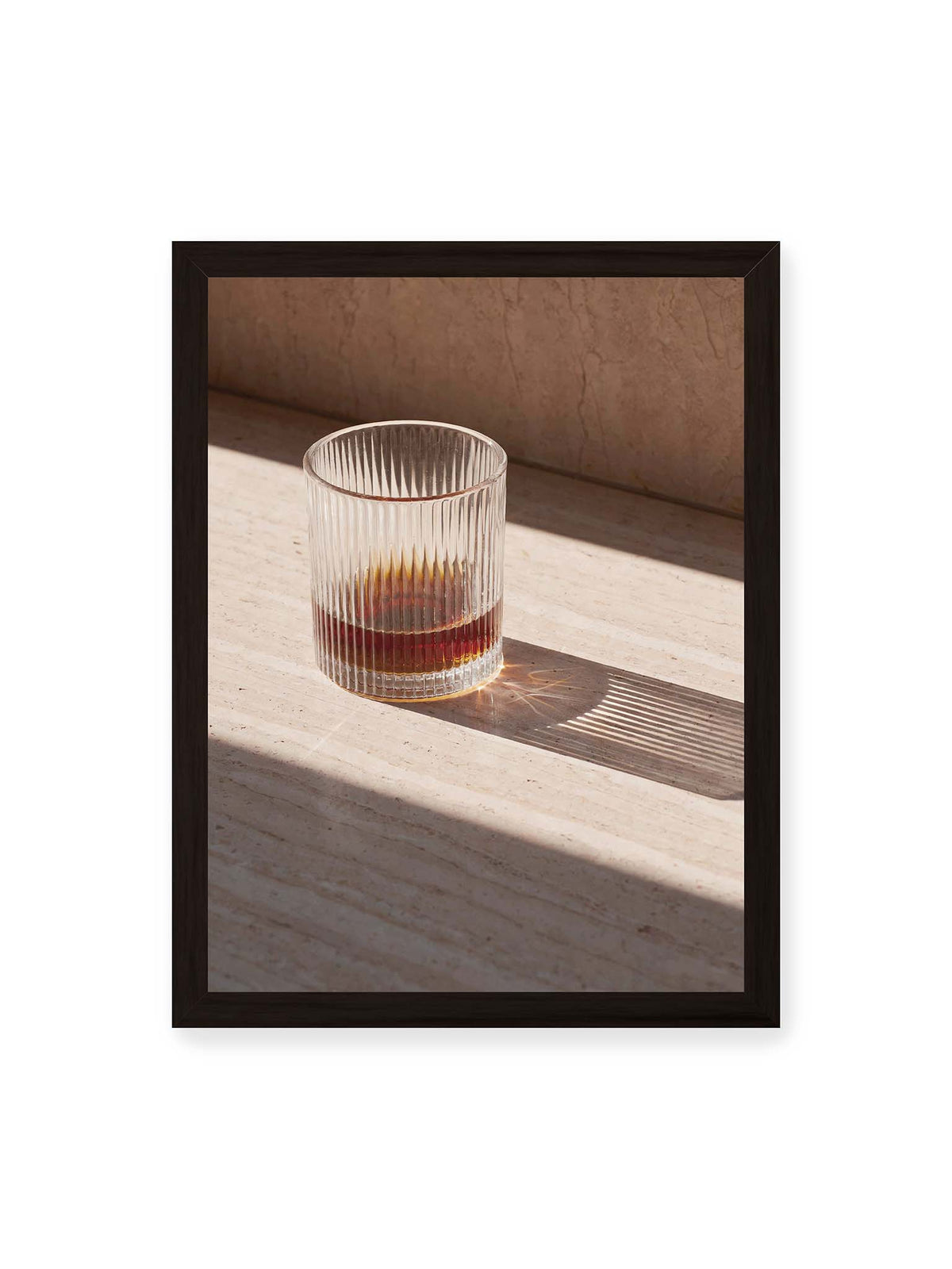 30x40 cm, schwarzer Rahmen – Geripptes Glas mit bernsteinfarbener Flüssigkeit auf heller Steinfläche im direkten Licht.