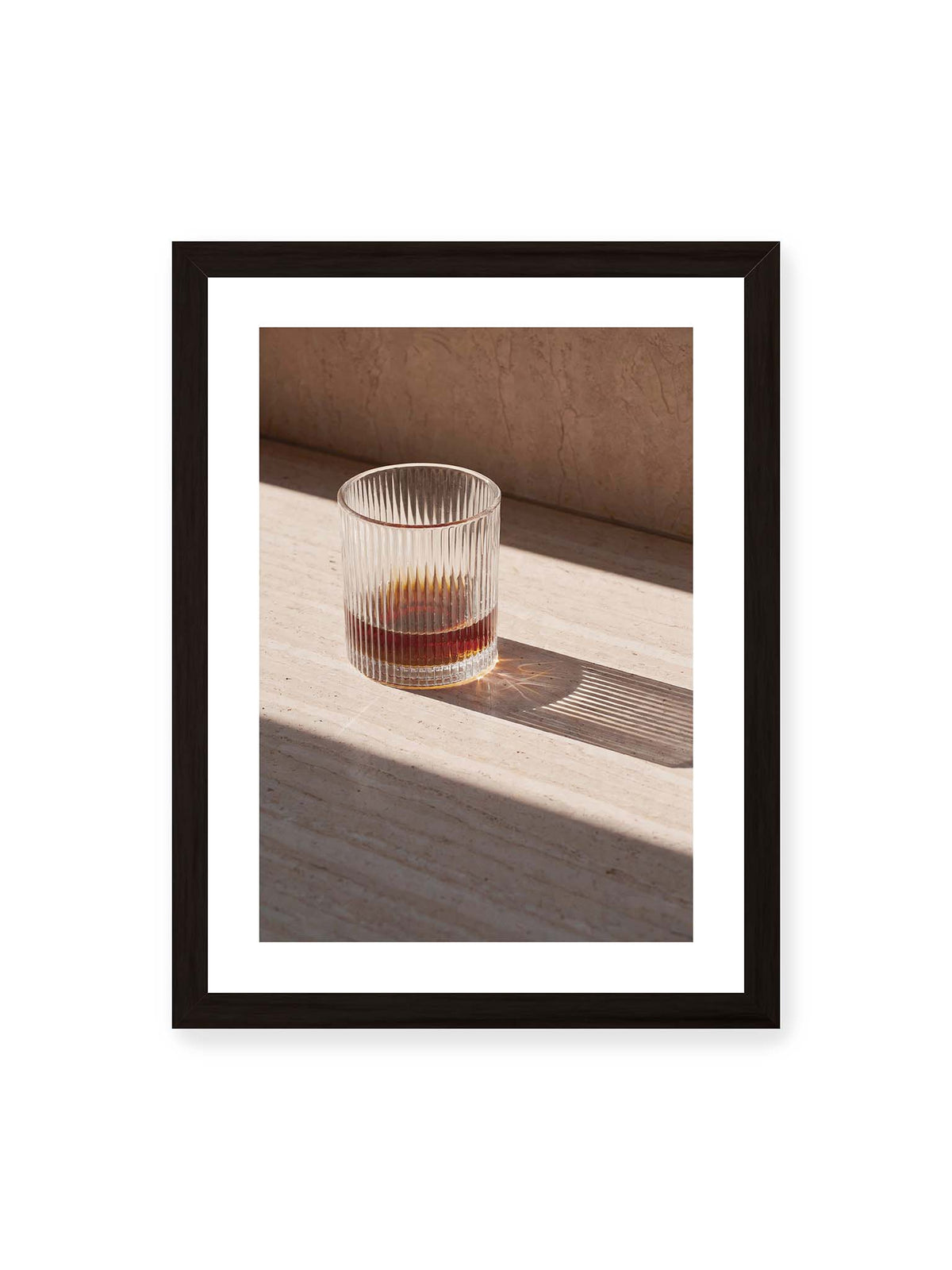 30x40 cm, weißer Galerie-Rand, schwarzer Rahmen – Geripptes Glas mit bernsteinfarbener Flüssigkeit auf heller Steinfläche im direkten Licht.