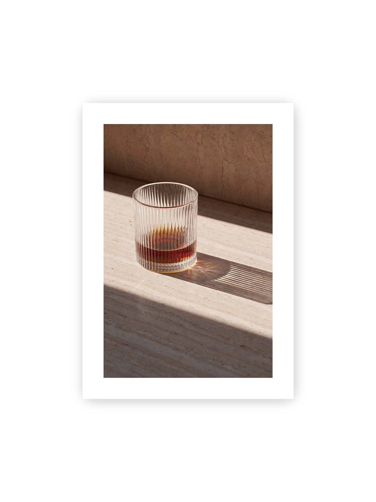 50x70 cm, weißer Galerie-Rand – Geripptes Glas mit bernsteinfarbener Flüssigkeit auf heller Steinfläche im direkten Licht.