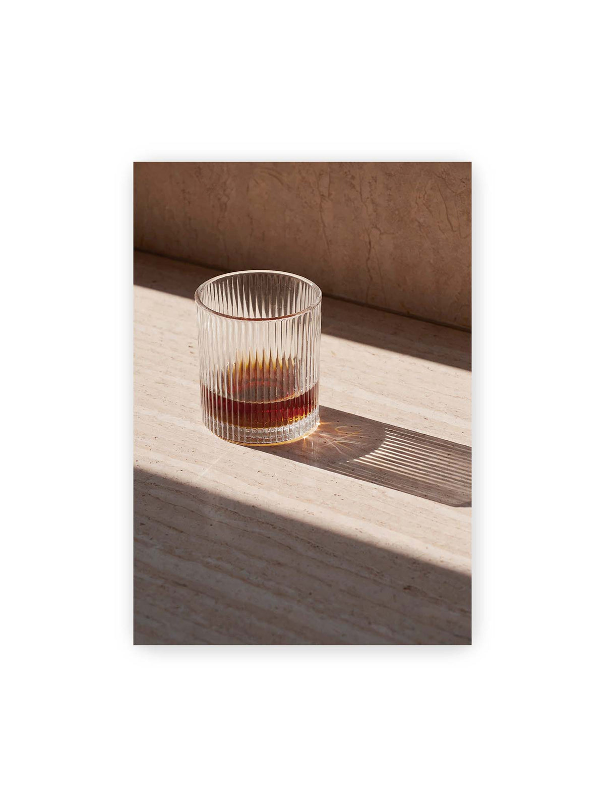 70x100 cm – Geripptes Glas mit bernsteinfarbener Flüssigkeit auf heller Steinfläche im direkten Licht.