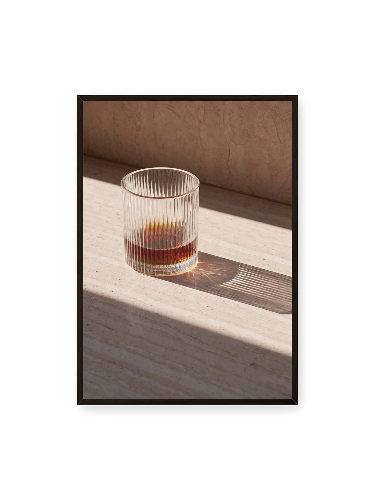 70x100 cm, schwarzer Rahmen – Geripptes Glas mit bernsteinfarbener Flüssigkeit auf heller Steinfläche im direkten Licht.