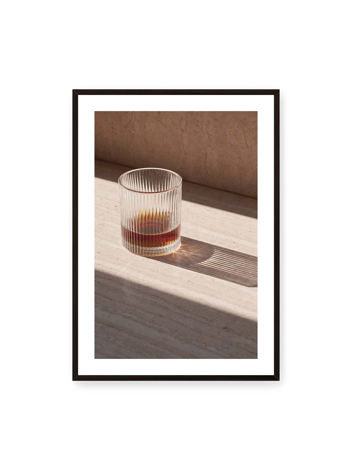 70x100 cm, weißer Galerie-Rand, schwarzer Rahmen – Geripptes Glas mit bernsteinfarbener Flüssigkeit auf heller Steinfläche im direkten Licht.