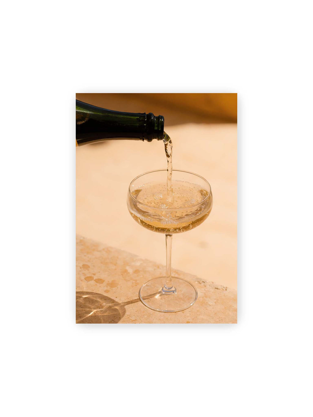 21x30 cm – Perlender Champagner wird aus einer dunklen Flasche in ein Coupéglas auf heller Steinfläche gegossen.