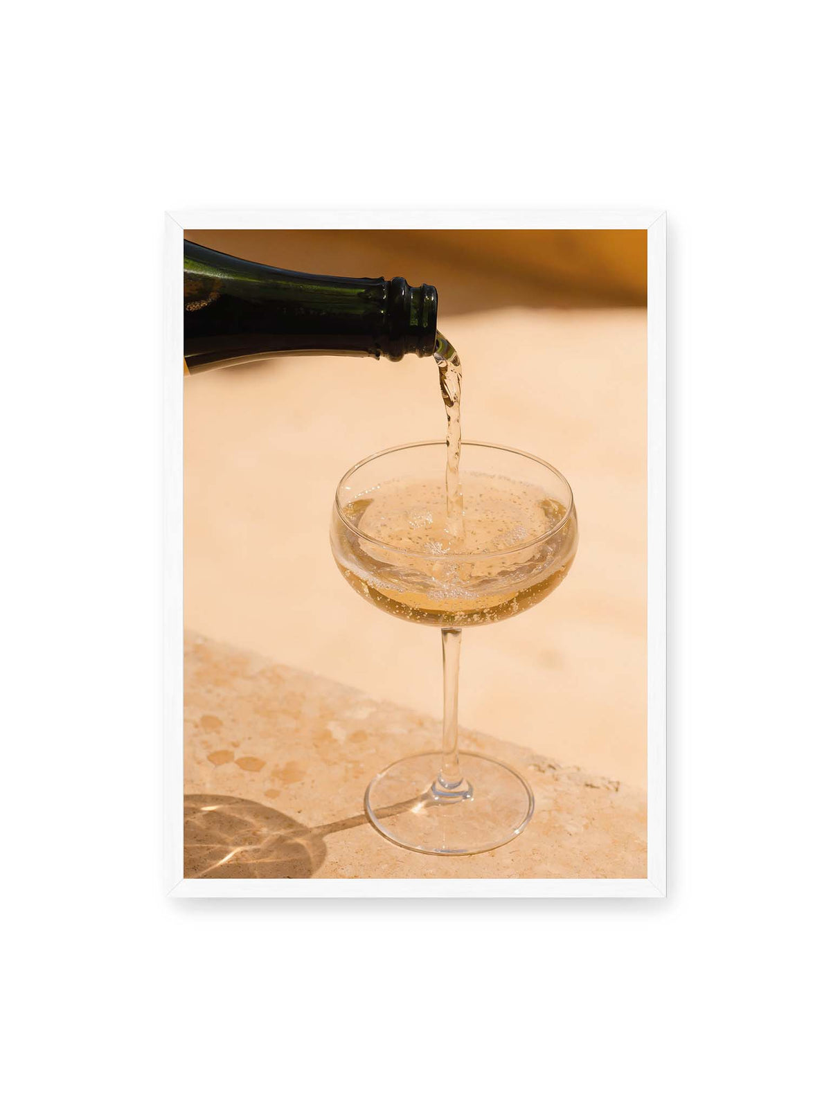 50x70 cm, weißer Rahmen – Perlender Champagner wird aus einer dunklen Flasche in ein Coupéglas auf heller Steinfläche gegossen.