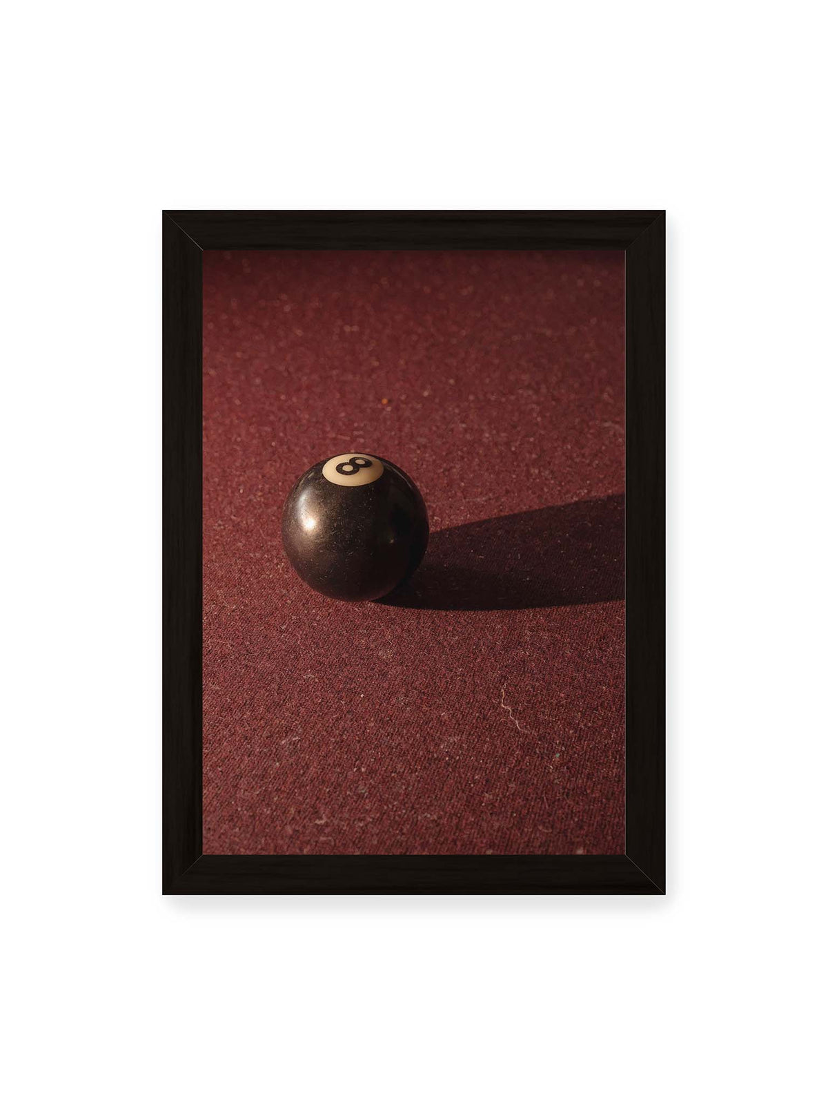 21x30 cm, schwarzer Rahmen – Schwarze Billardkugel auf tiefroter Spielfläche mit langem Schatten im seitlichen Licht.