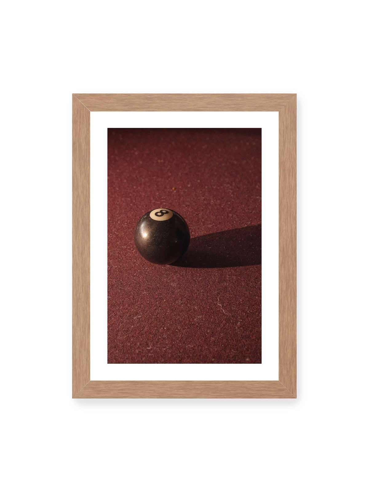 21x30 cm, weißer Galerie-Rand, Eichenrahmen – Schwarze Billardkugel auf tiefroter Spielfläche mit langem Schatten im seitlichen Licht.
