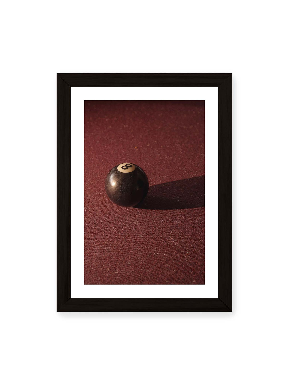 21x30 cm, weißer Galerie-Rand, schwarzer Rahmen – Schwarze Billardkugel auf tiefroter Spielfläche mit langem Schatten im seitlichen Licht.