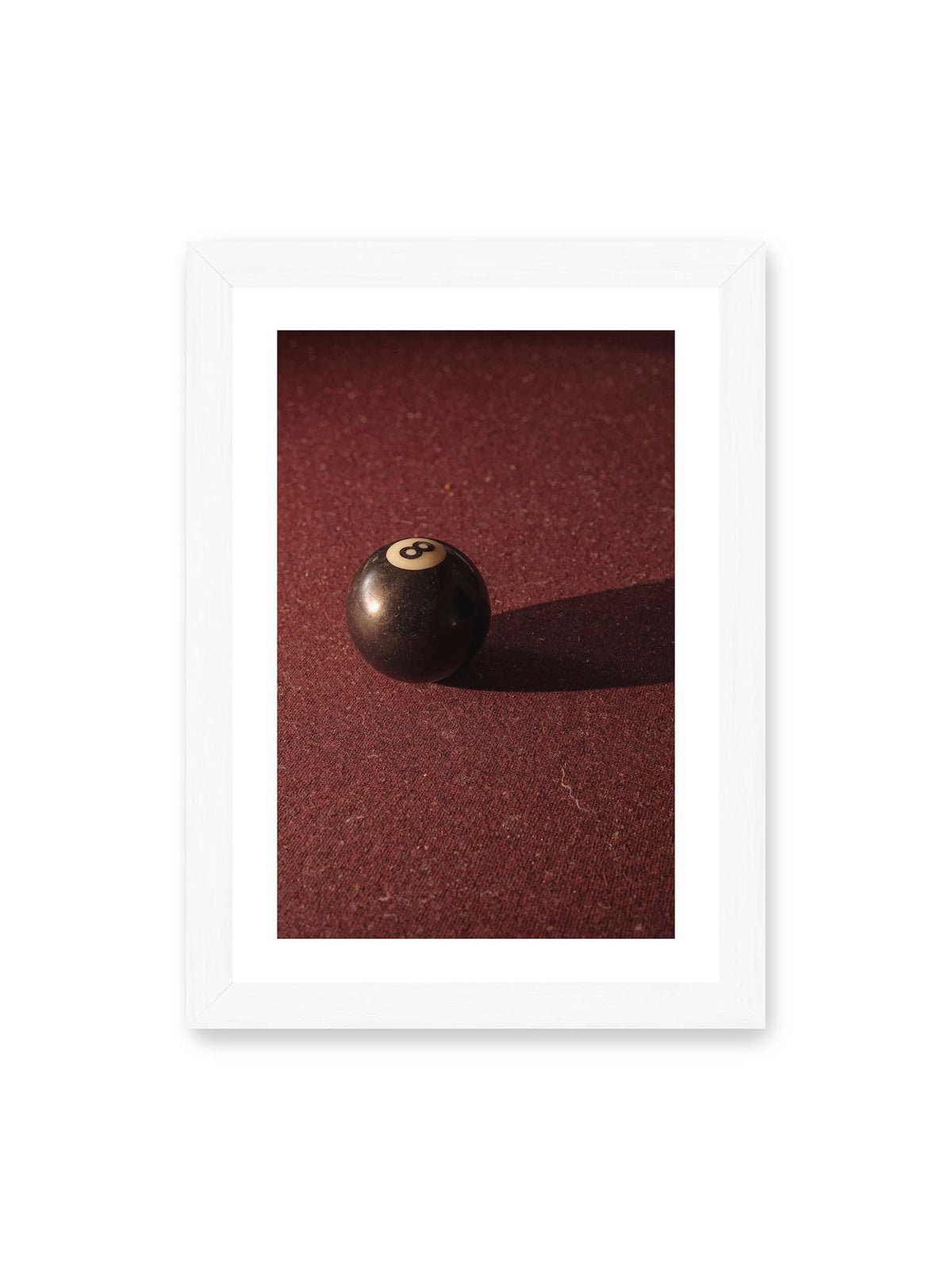 21x30 cm, weißer Galerie-Rand, weißer Rahmen – Schwarze Billardkugel auf tiefroter Spielfläche mit langem Schatten im seitlichen Licht.