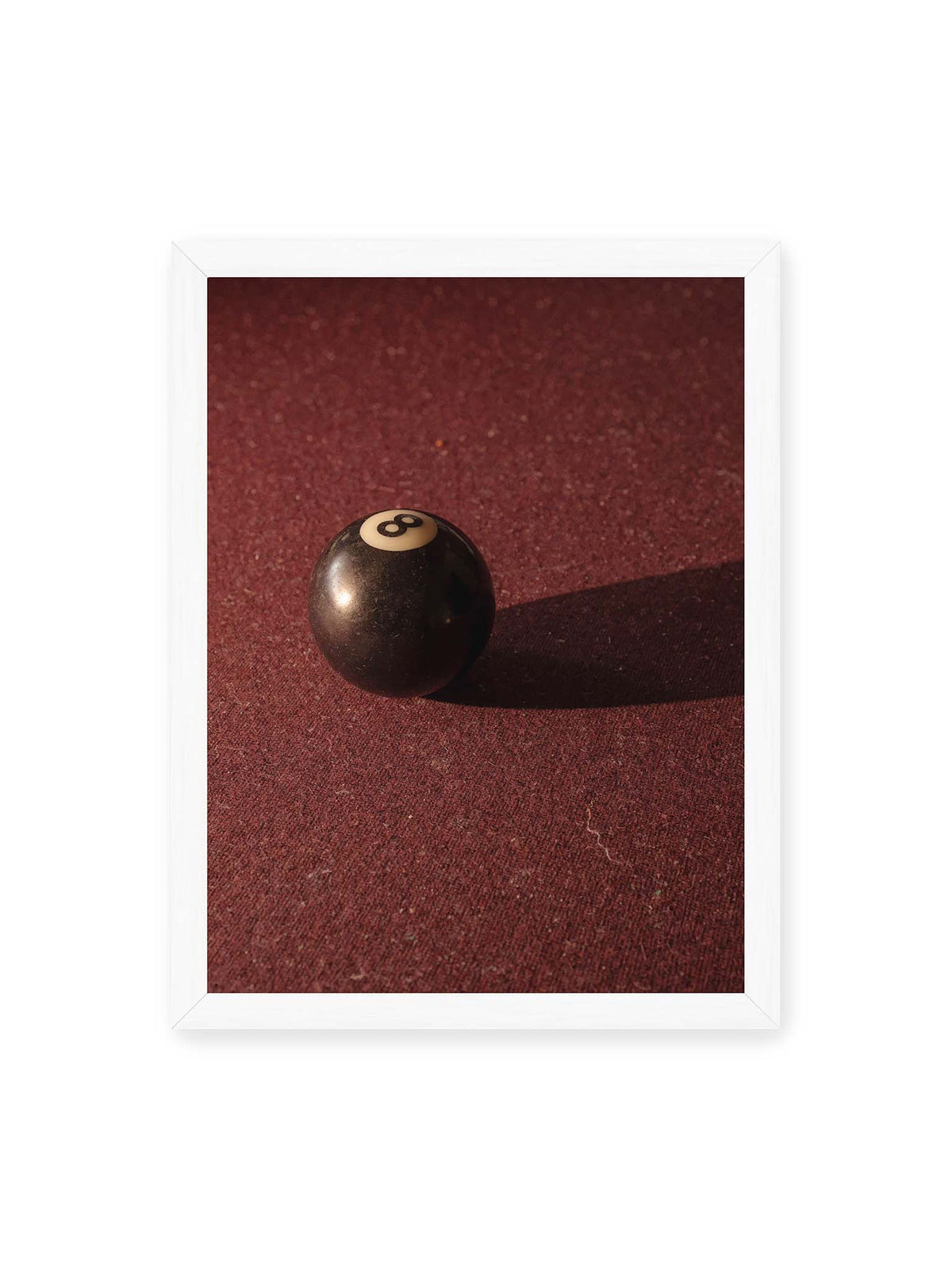 30x40 cm, weißer Rahmen – Schwarze Billardkugel auf tiefroter Spielfläche mit langem Schatten im seitlichen Licht.