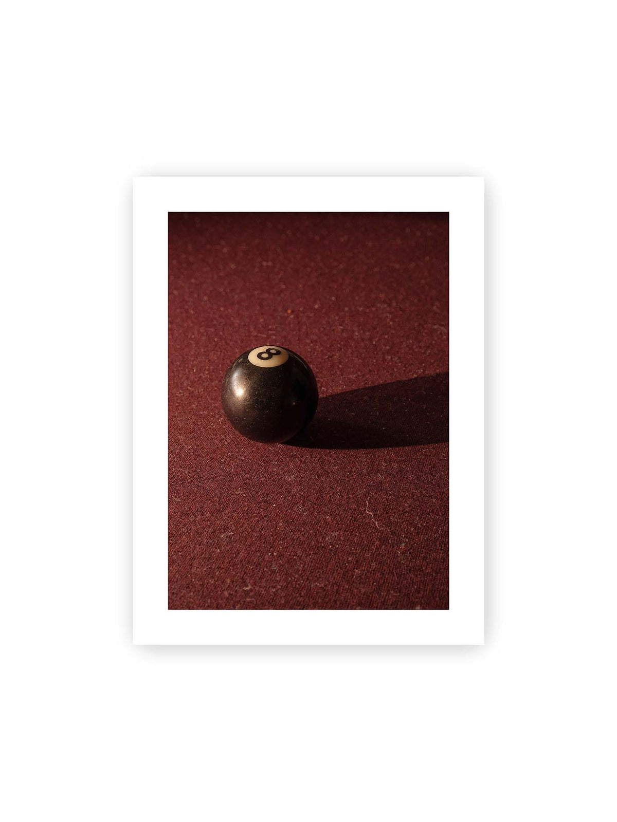 30x40 cm, weißer Galerie-Rand – Schwarze Billardkugel auf tiefroter Spielfläche mit langem Schatten im seitlichen Licht.