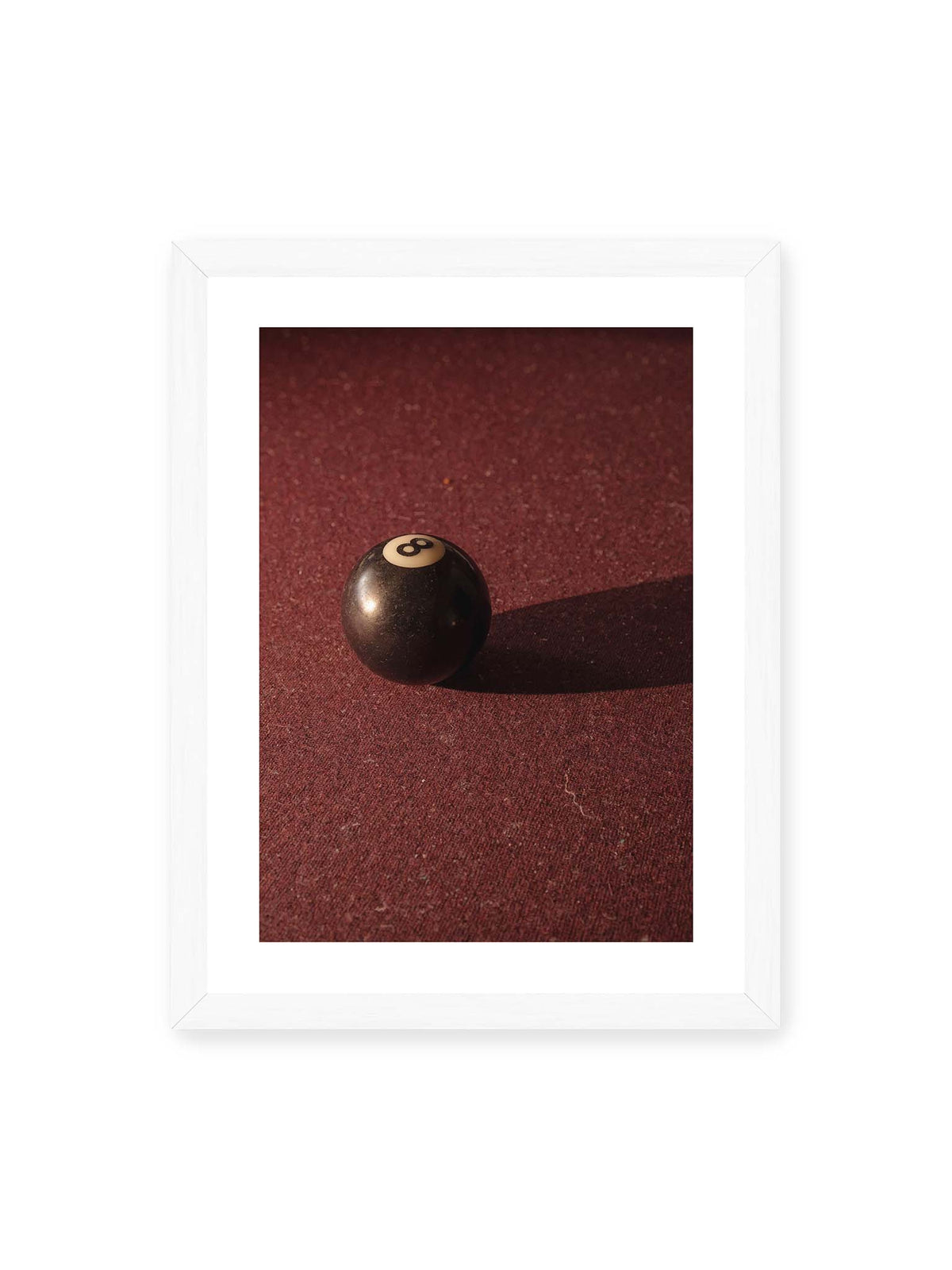 30x40 cm, weißer Galerie-Rand, weißer Rahmen – Schwarze Billardkugel auf tiefroter Spielfläche mit langem Schatten im seitlichen Licht.