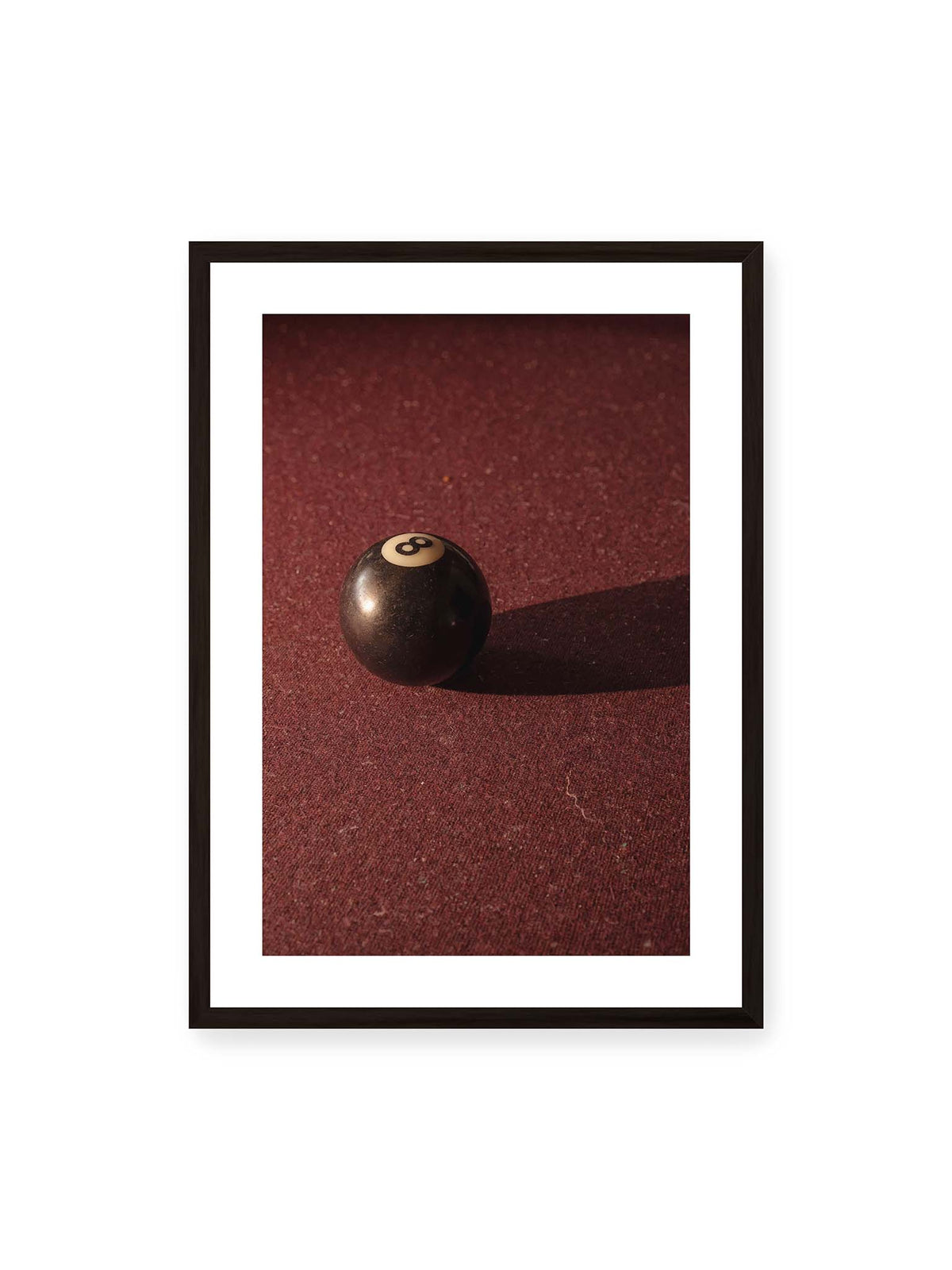 50x70 cm, weißer Galerie-Rand, schwarzer Rahmen – Schwarze Billardkugel auf tiefroter Spielfläche mit langem Schatten im seitlichen Licht.