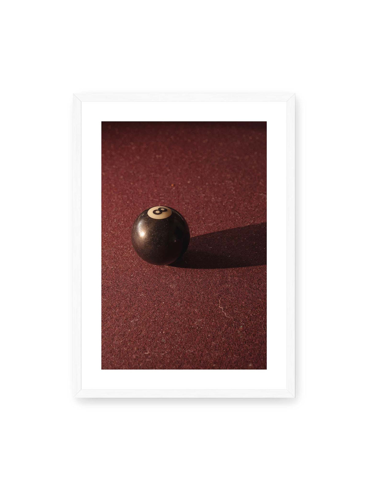 50x70 cm, weißer Galerie-Rand, weißer Rahmen – Schwarze Billardkugel auf tiefroter Spielfläche mit langem Schatten im seitlichen Licht.