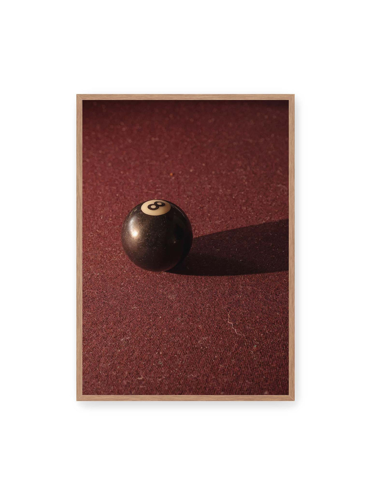 70x100 cm, Eichenrahmen – Schwarze Billardkugel auf tiefroter Spielfläche mit langem Schatten im seitlichen Licht.