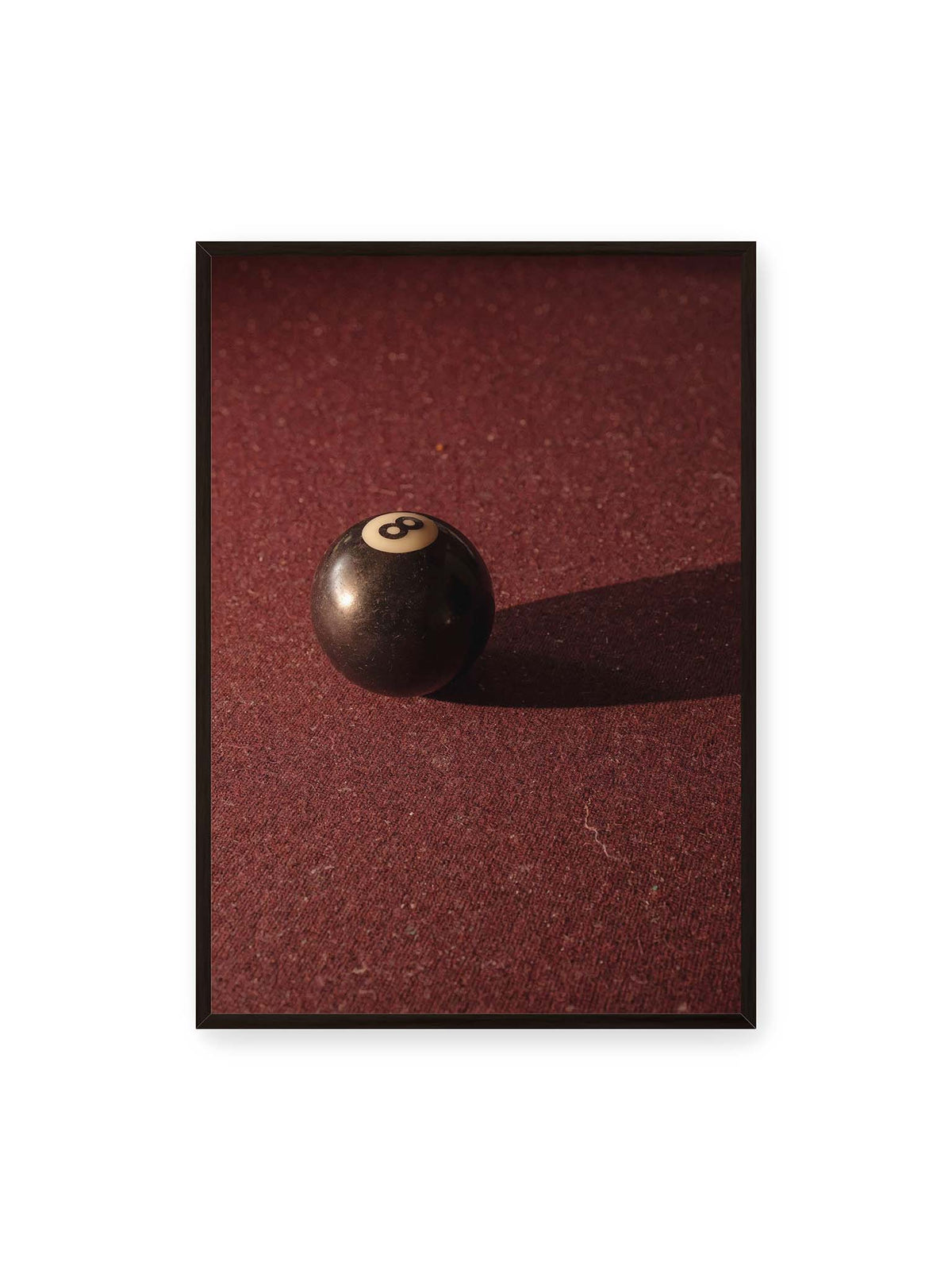 70x100 cm, schwarzer Rahmen – Schwarze Billardkugel auf tiefroter Spielfläche mit langem Schatten im seitlichen Licht.