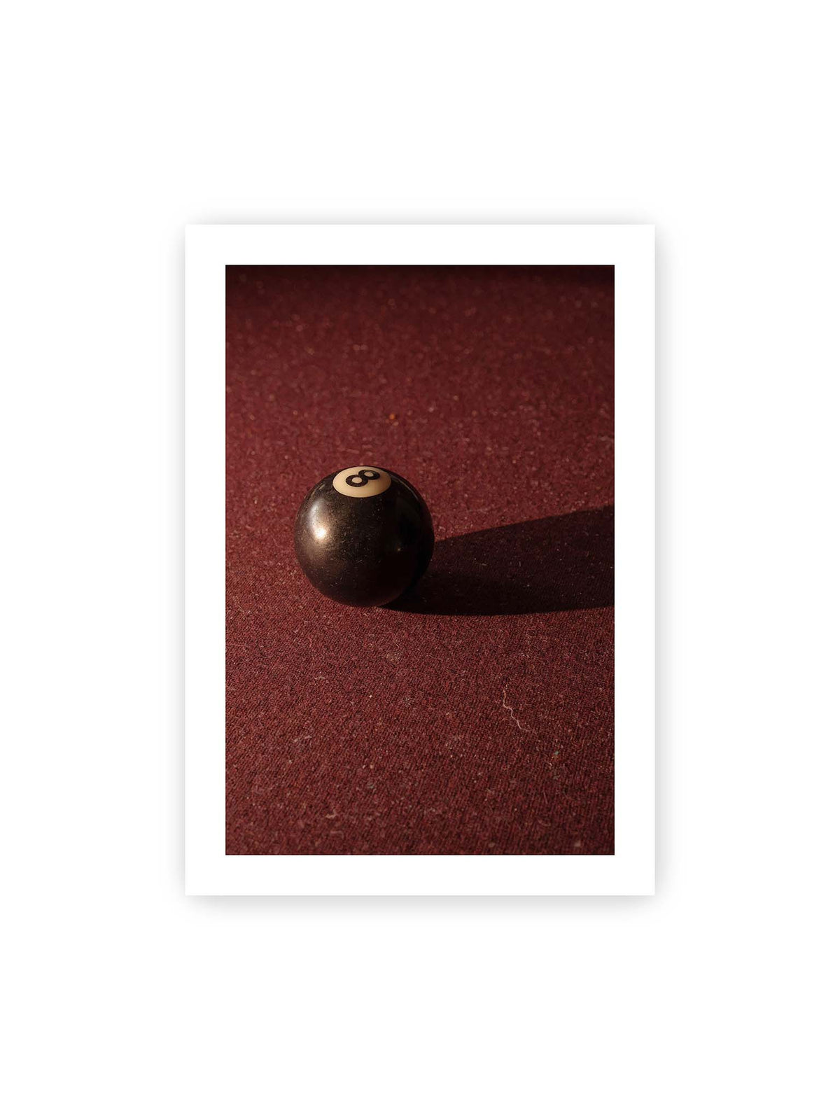 70x100 cm, weißer Galerie-Rand – Schwarze Billardkugel auf tiefroter Spielfläche mit langem Schatten im seitlichen Licht.