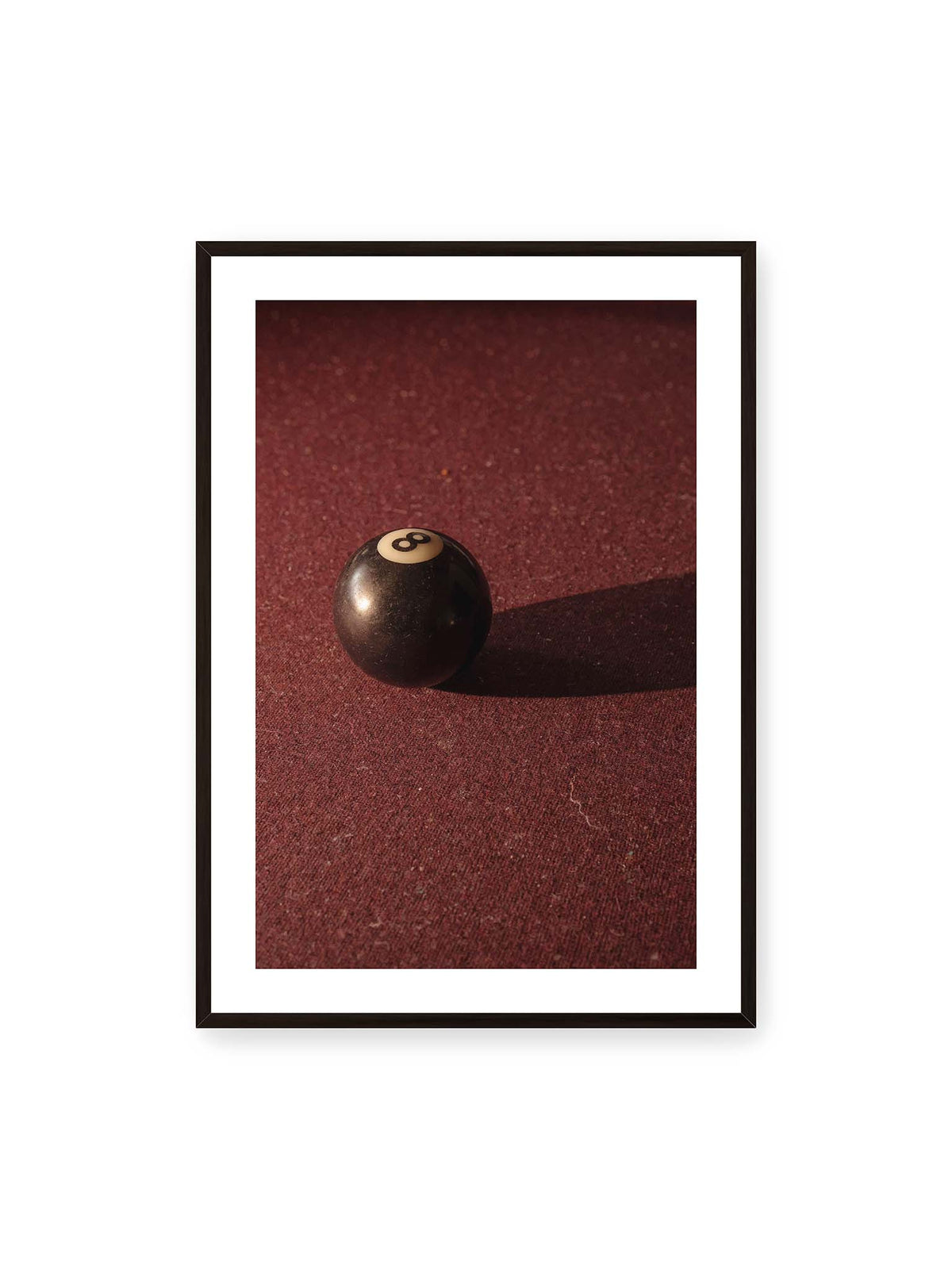 70x100 cm, weißer Galerie-Rand, schwarzer Rahmen – Schwarze Billardkugel auf tiefroter Spielfläche mit langem Schatten im seitlichen Licht.