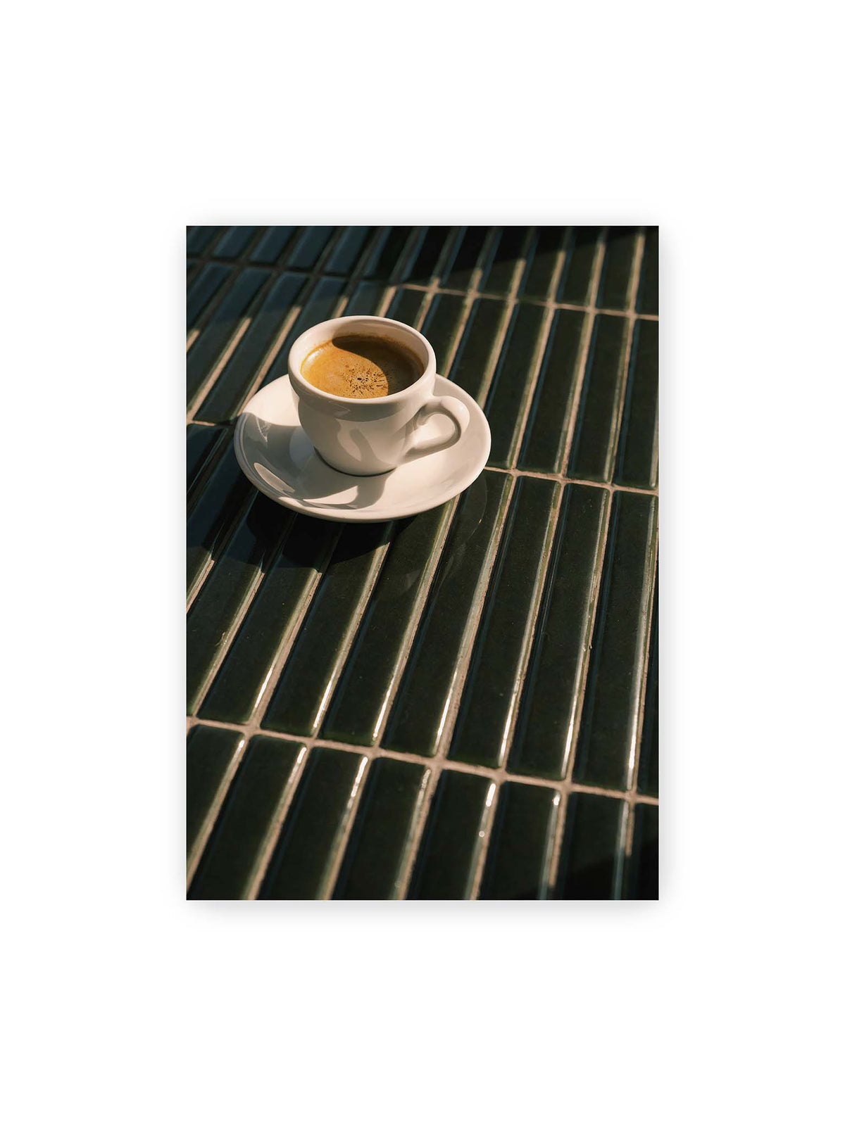 70x100 cm – Weiße Espressotasse auf dunkelgrünen Fliesen im direkten Licht mit geometrischen Schatten.