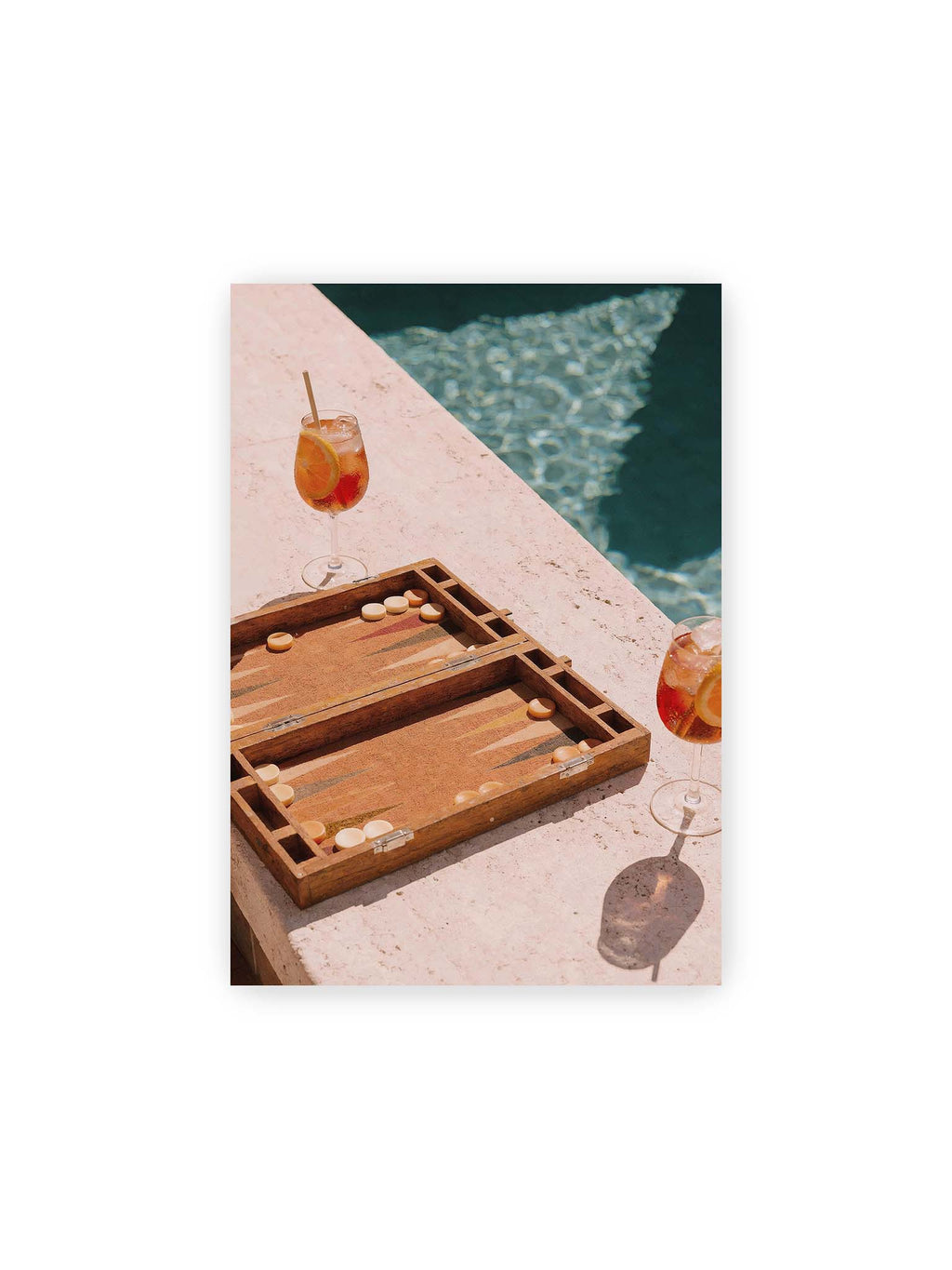 21x30 cm – Geöffnetes Backgammonbrett mit zwei orangefarbenen Drinks auf heller Steinfläche neben blauem Wasser.