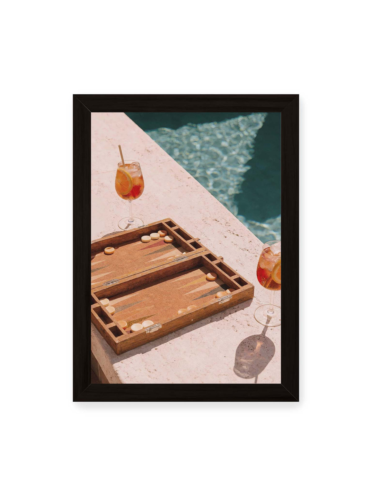 21x30 cm, schwarzer Rahmen – Geöffnetes Backgammonbrett mit zwei orangefarbenen Drinks auf heller Steinfläche neben blauem Wasser.