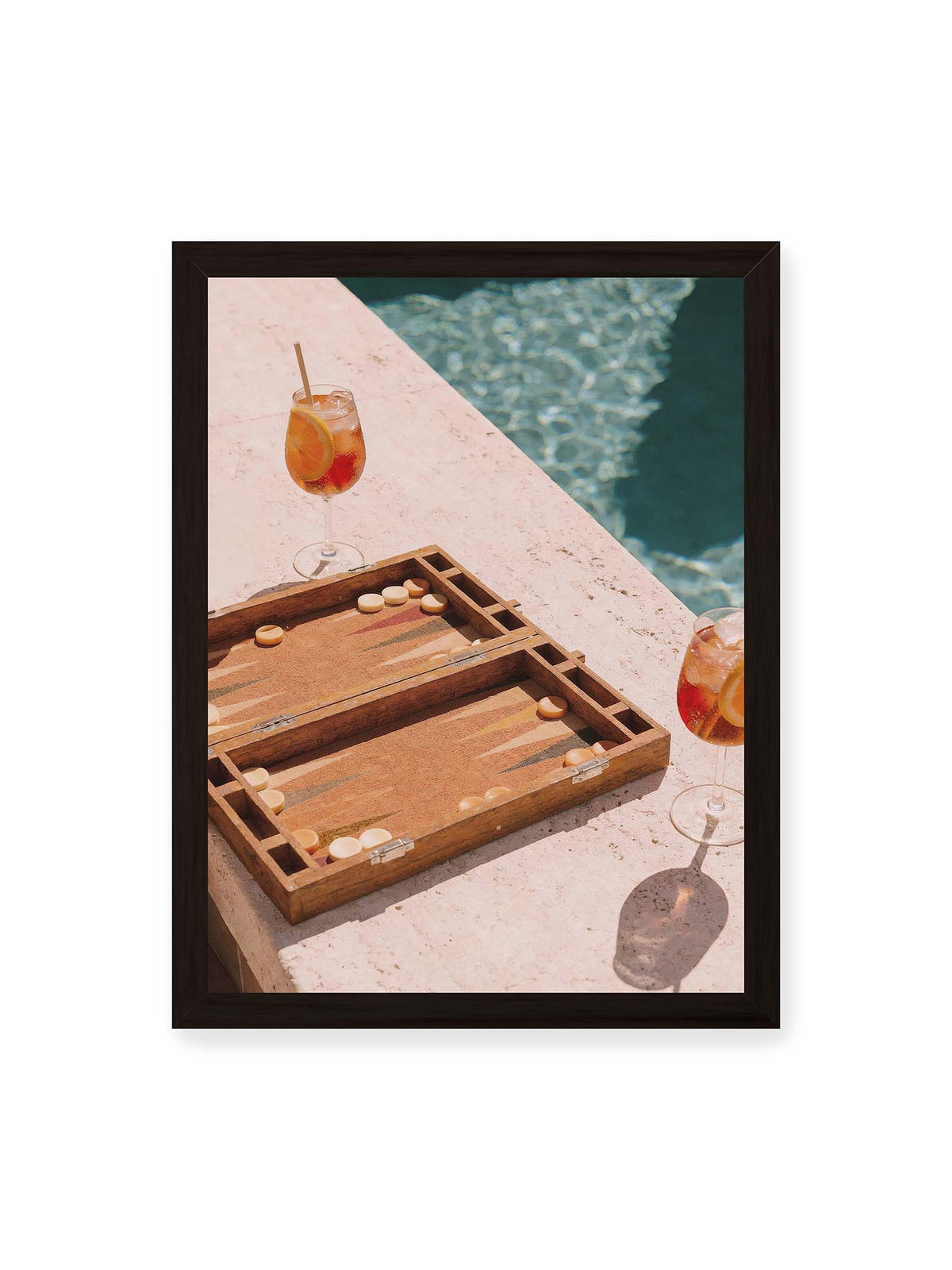 30x40 cm, schwarzer Rahmen – Geöffnetes Backgammonbrett mit zwei orangefarbenen Drinks auf heller Steinfläche neben blauem Wasser.