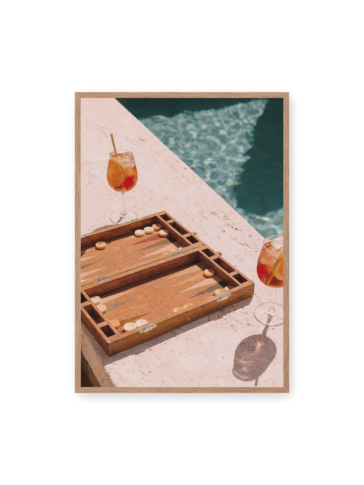 70x100 cm, Eichenrahmen – Geöffnetes Backgammonbrett mit zwei orangefarbenen Drinks auf heller Steinfläche neben blauem Wasser.