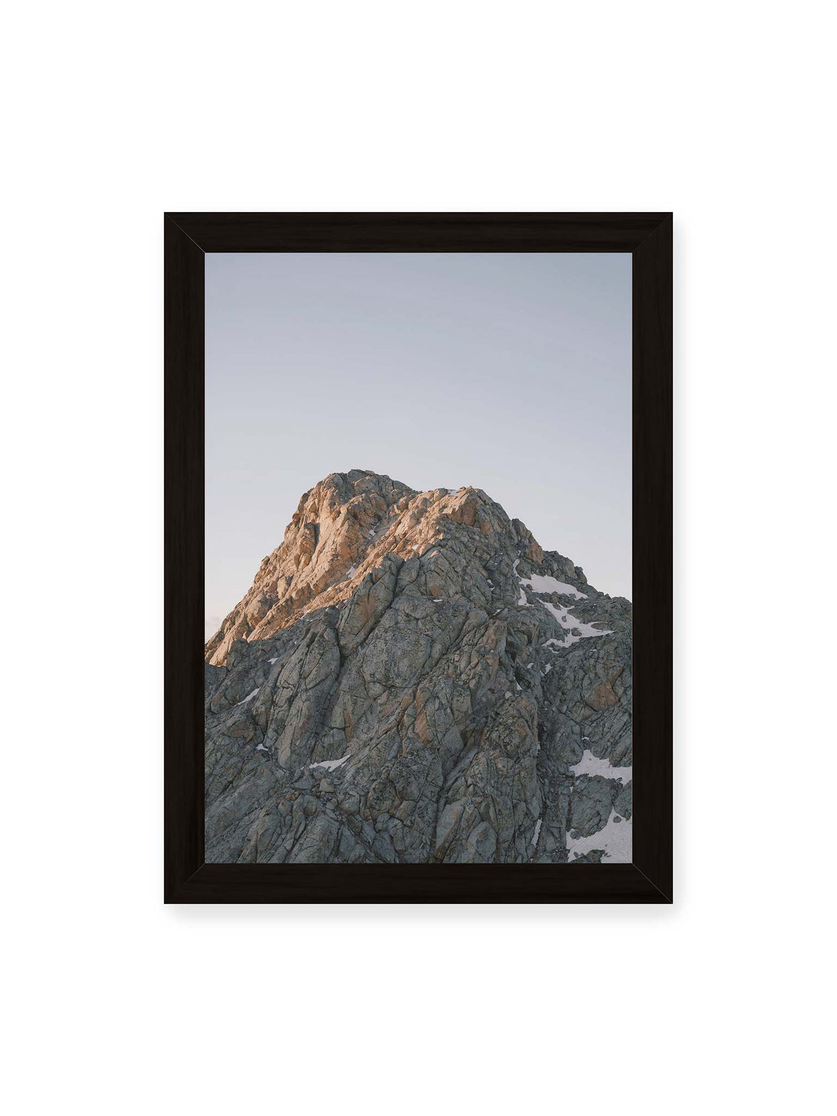 21x30 cm, schwarzer Rahmen – Massiver grauer Felsgipfel mit kleinen Schneefeldern vor einem weiten blassblauen Himmel.