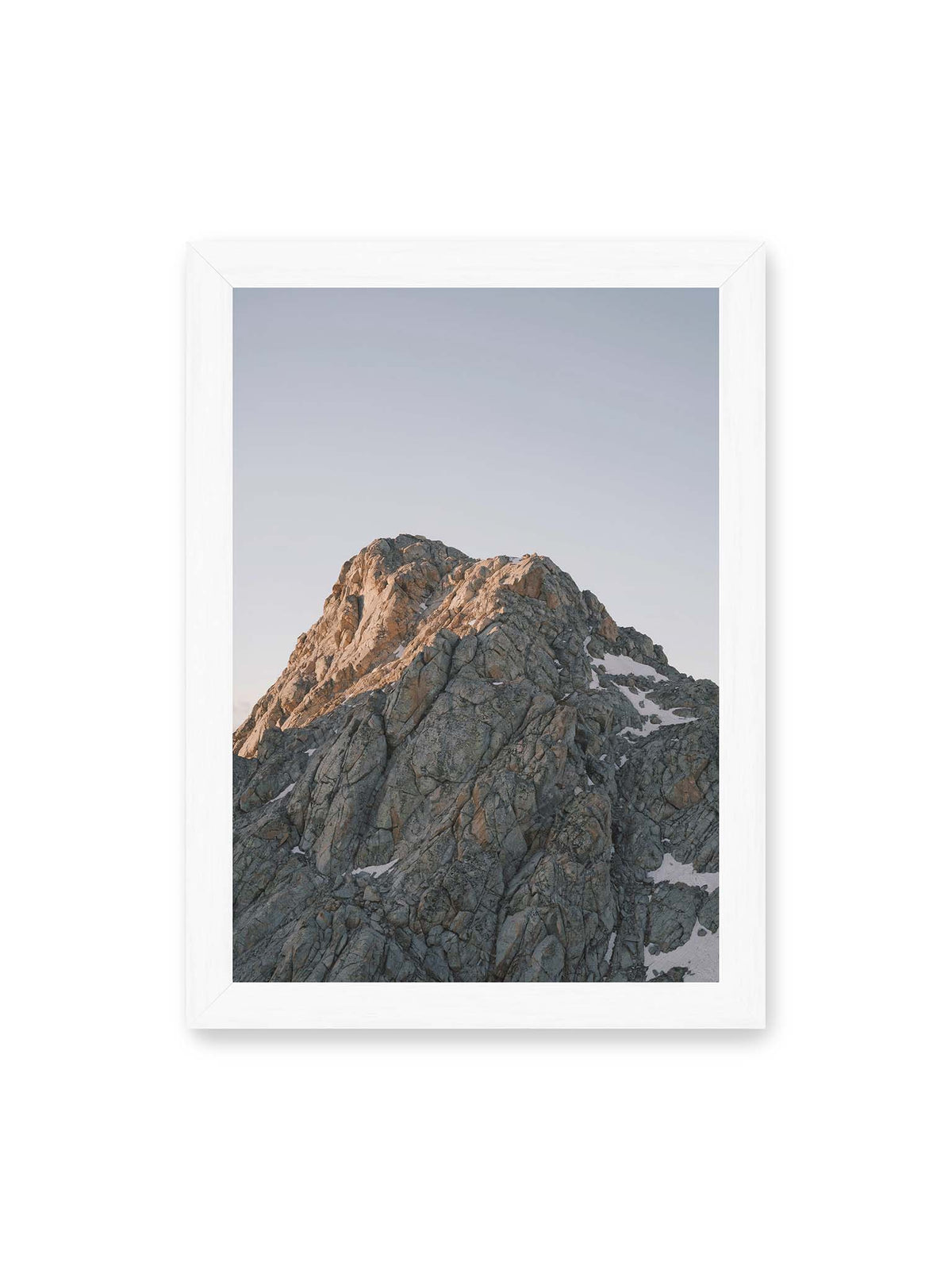 21x30 cm, weißer Rahmen – Massiver grauer Felsgipfel mit kleinen Schneefeldern vor einem weiten blassblauen Himmel.