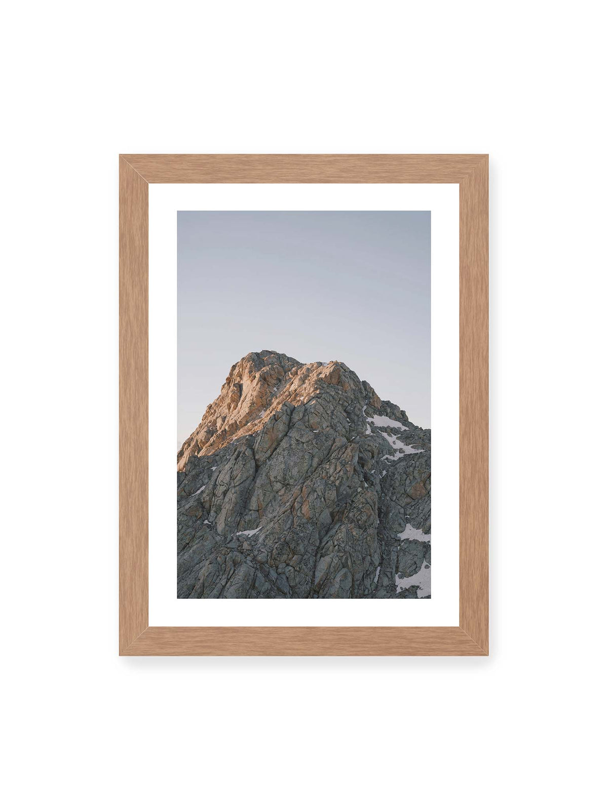 21x30 cm, weißer Galerie-Rand, Eichenrahmen – Massiver grauer Felsgipfel mit kleinen Schneefeldern vor einem weiten blassblauen Himmel.