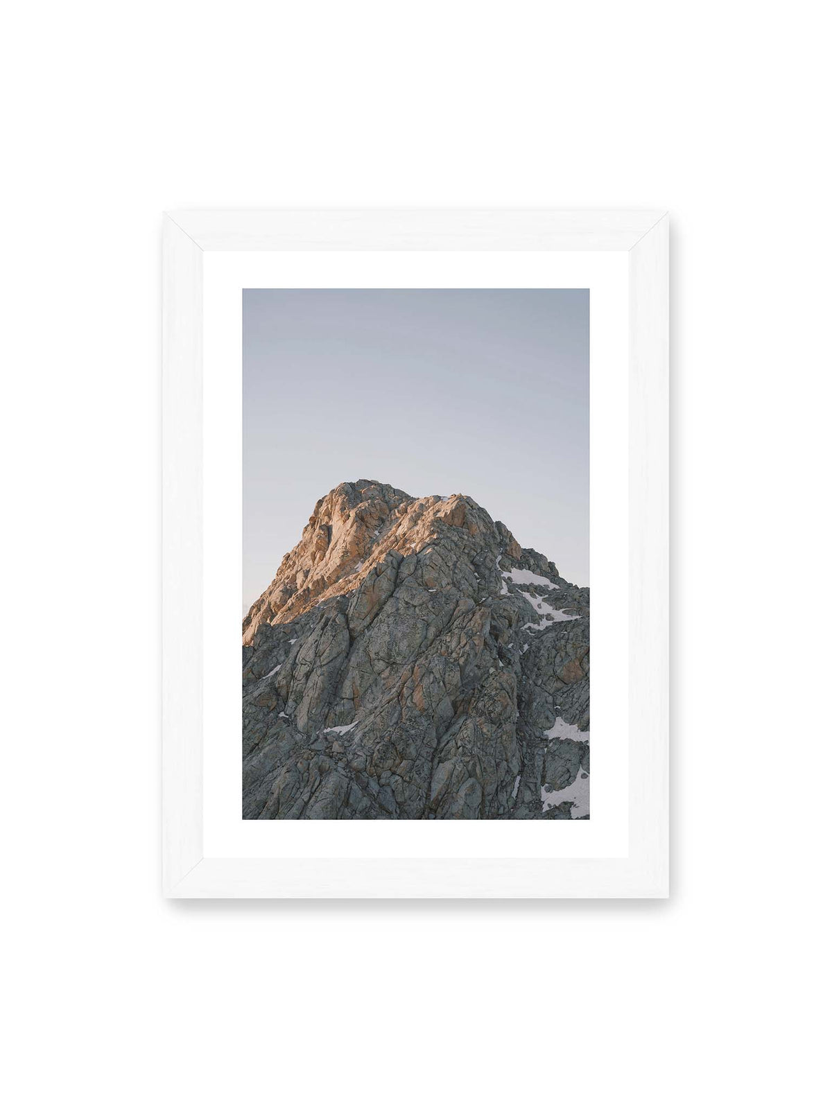 21x30 cm, weißer Galerie-Rand, weißer Rahmen – Massiver grauer Felsgipfel mit kleinen Schneefeldern vor einem weiten blassblauen Himmel.