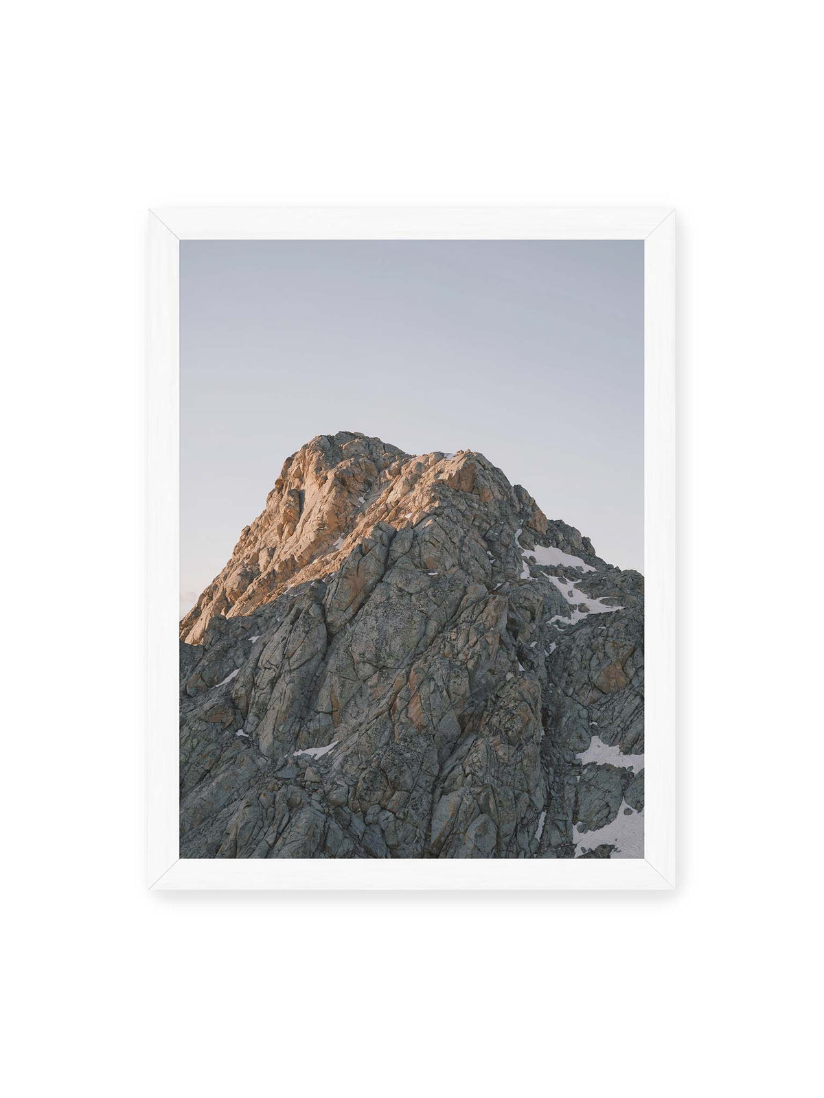 30x40 cm, weißer Rahmen – Massiver grauer Felsgipfel mit kleinen Schneefeldern vor einem weiten blassblauen Himmel.