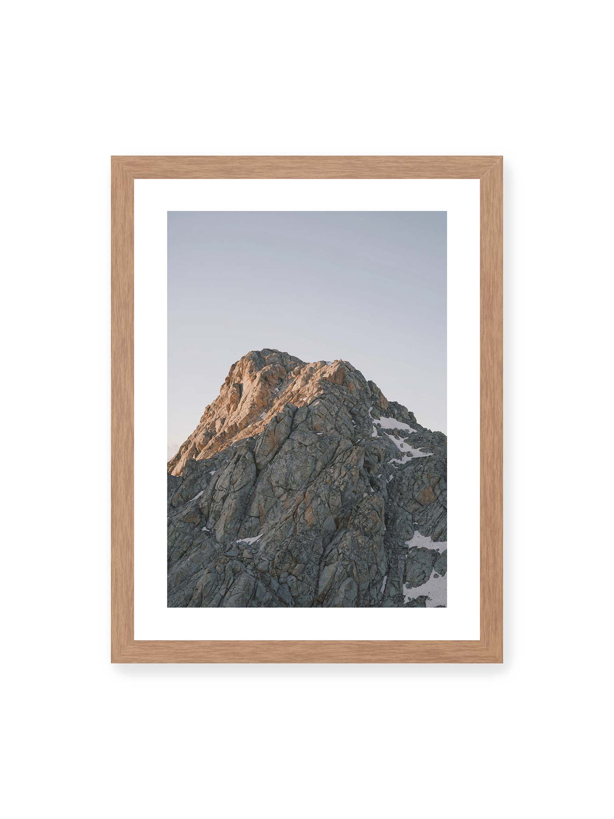 30x40 cm, weißer Galerie-Rand, Eichenrahmen – Massiver grauer Felsgipfel mit kleinen Schneefeldern vor einem weiten blassblauen Himmel.