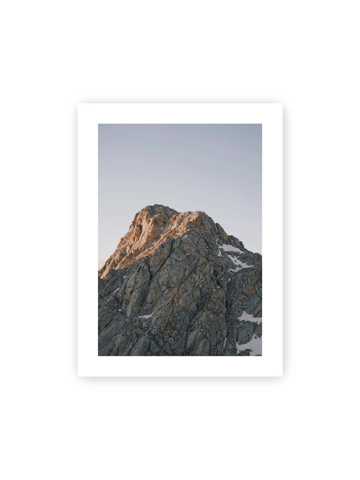 30x40 cm, weißer Galerie-Rand – Massiver grauer Felsgipfel mit kleinen Schneefeldern vor einem weiten blassblauen Himmel.