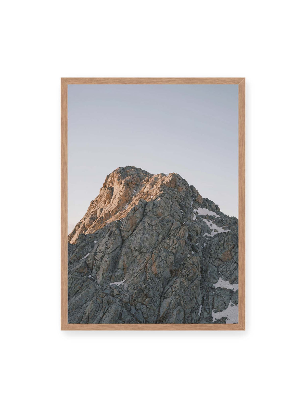50x70 cm, Eichenrahmen – Massiver grauer Felsgipfel mit kleinen Schneefeldern vor einem weiten blassblauen Himmel.