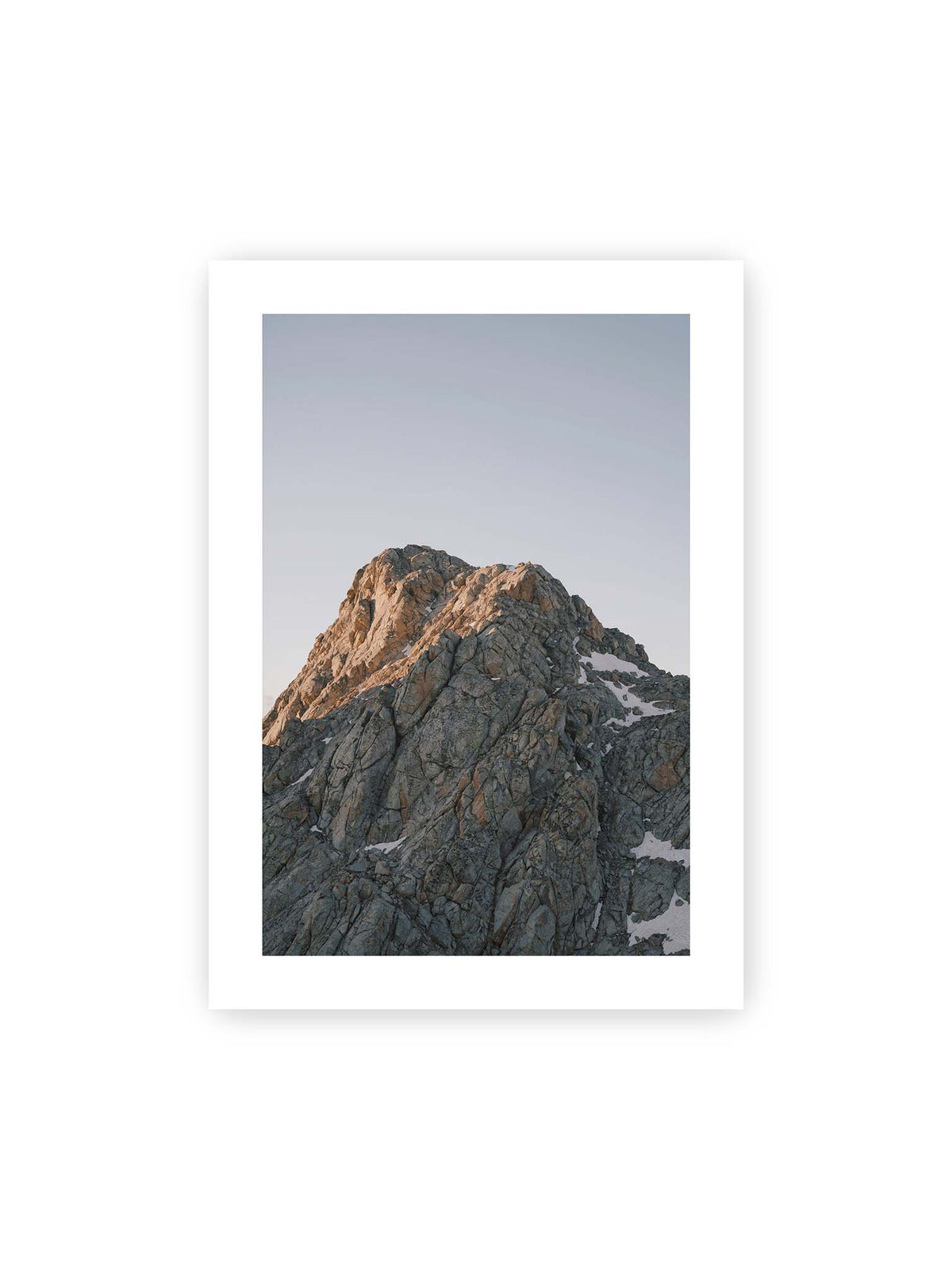 50x70 cm, weißer Galerie-Rand – Massiver grauer Felsgipfel mit kleinen Schneefeldern vor einem weiten blassblauen Himmel.