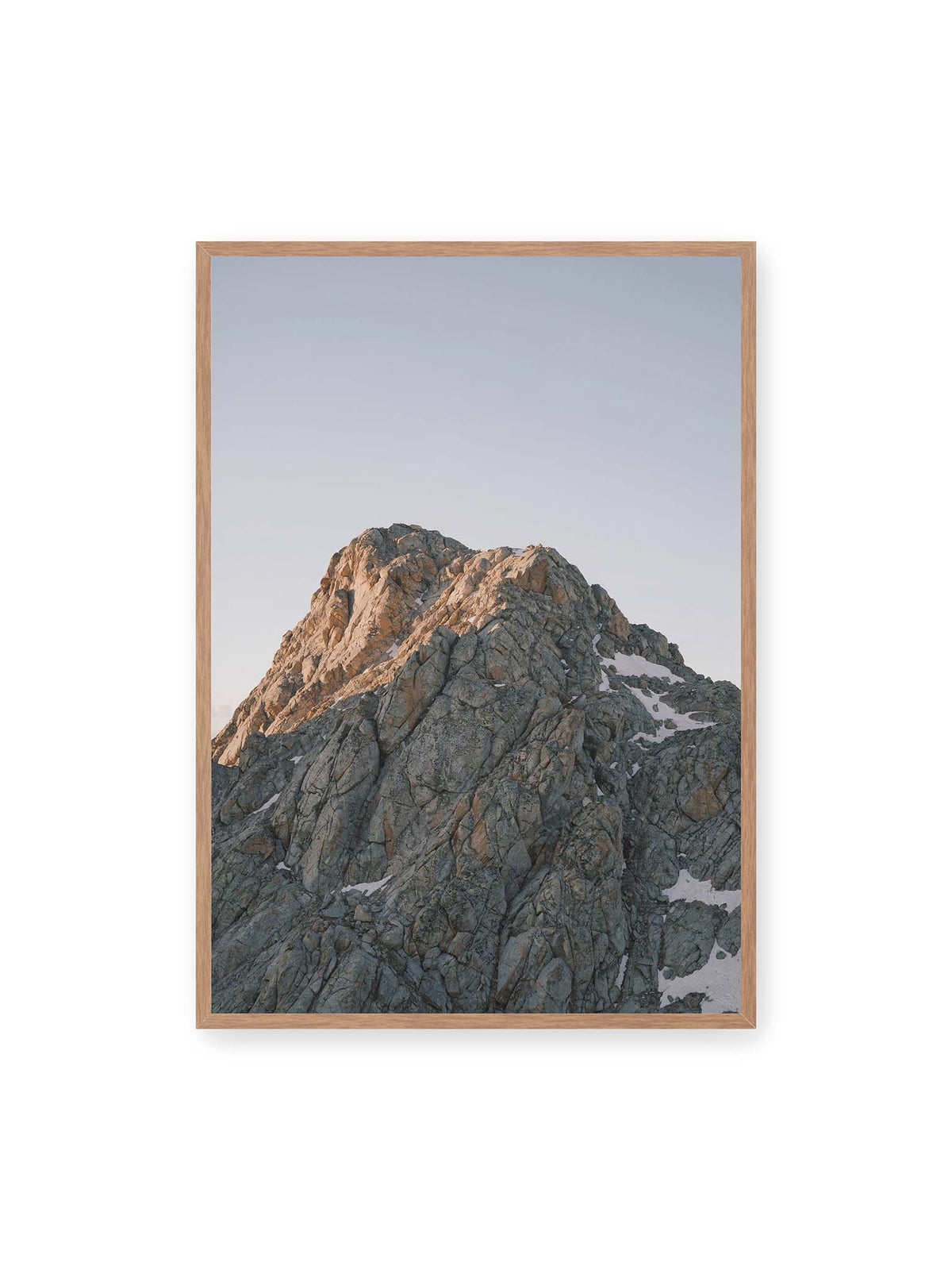 70x100 cm, Eichenrahmen – Massiver grauer Felsgipfel mit kleinen Schneefeldern vor einem weiten blassblauen Himmel.
