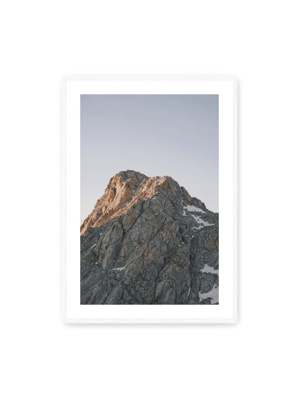 70x100 cm, weißer Galerie-Rand, weißer Rahmen – Massiver grauer Felsgipfel mit kleinen Schneefeldern vor einem weiten blassblauen Himmel.