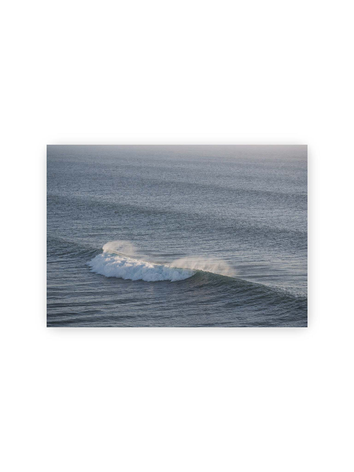 30x21 cm – Brechende Welle mit weißem Schaum und feiner Gischt auf einer weiten blau-grauen Wasserfläche.