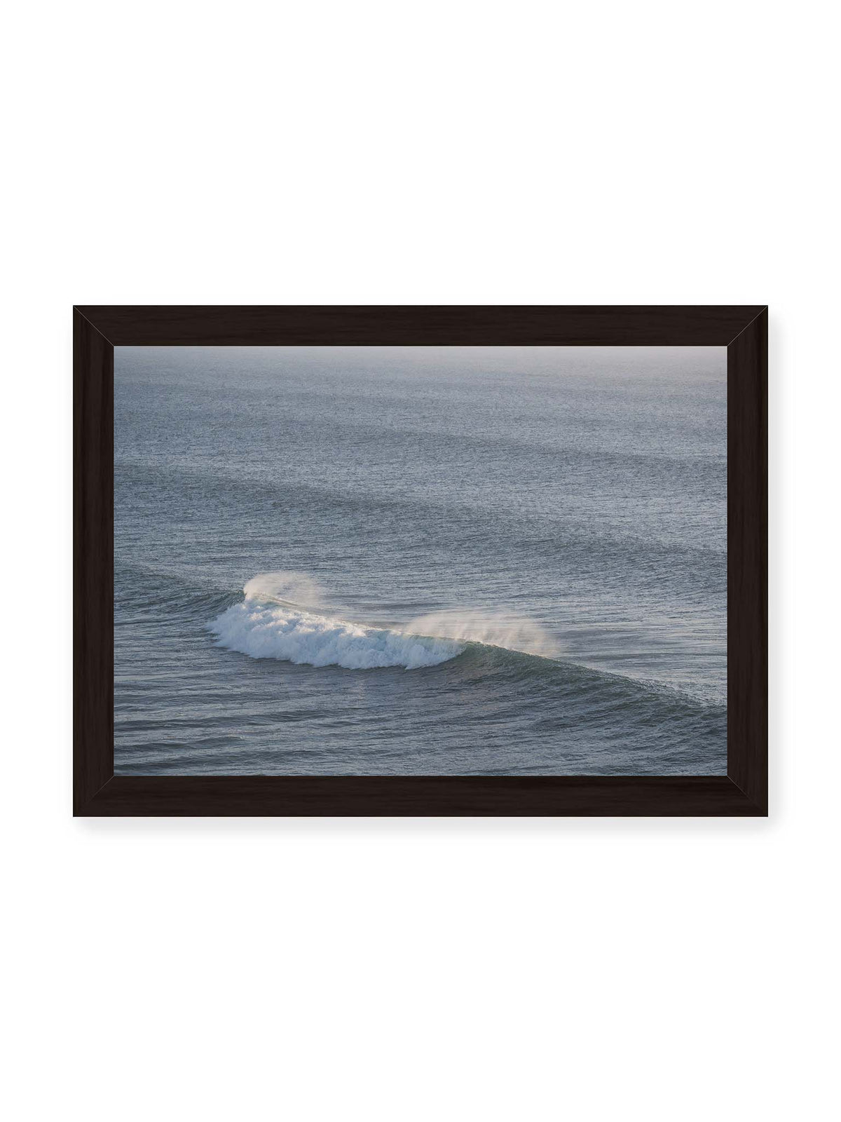 30x21 cm, schwarzer Rahmen – Brechende Welle mit weißem Schaum und feiner Gischt auf einer weiten blau-grauen Wasserfläche.