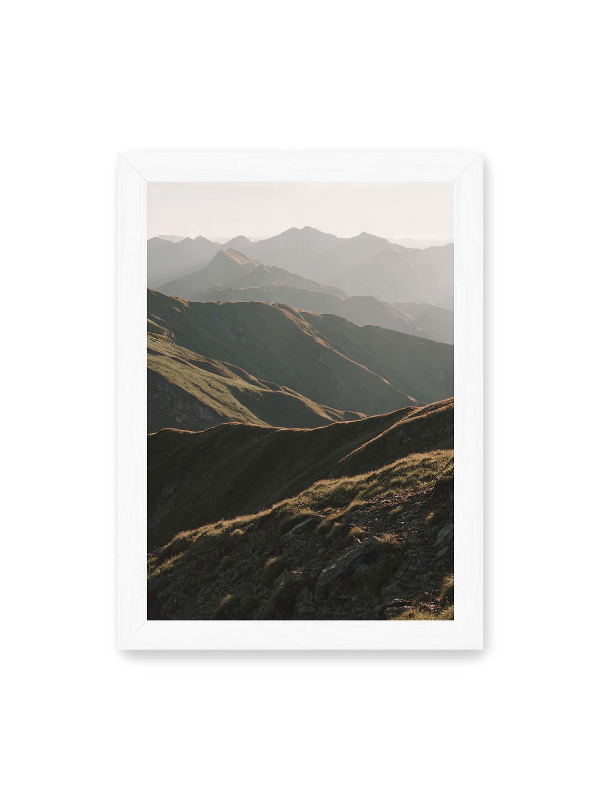 21x30 cm, weißer Rahmen – Gestaffelte Bergketten mit grasbewachsenen Hängen und warm beleuchteten Konturen unter hellem Himmel.