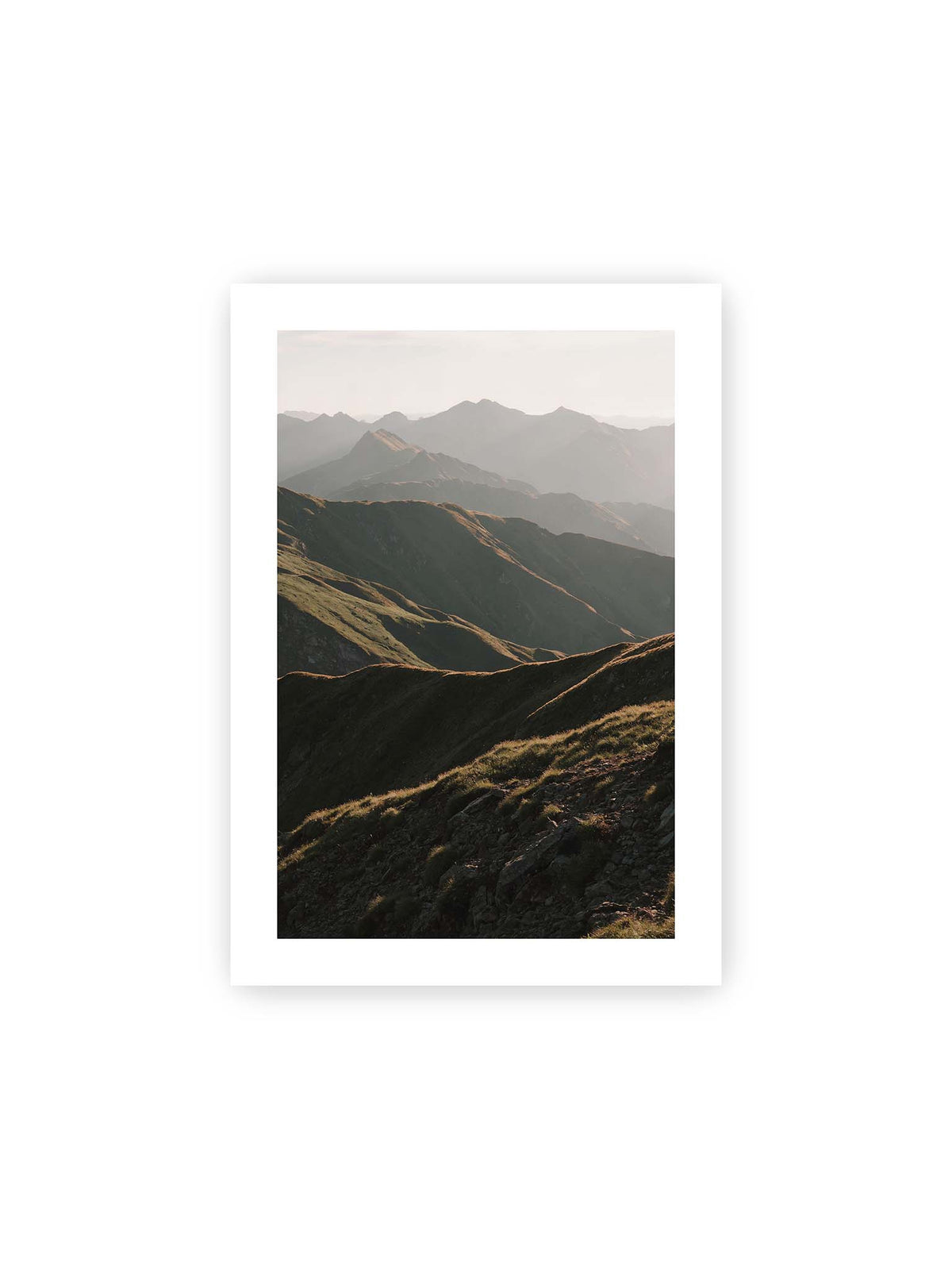 21x30 cm, weißer Galerie-Rand – Gestaffelte Bergketten mit grasbewachsenen Hängen und warm beleuchteten Konturen unter hellem Himmel.