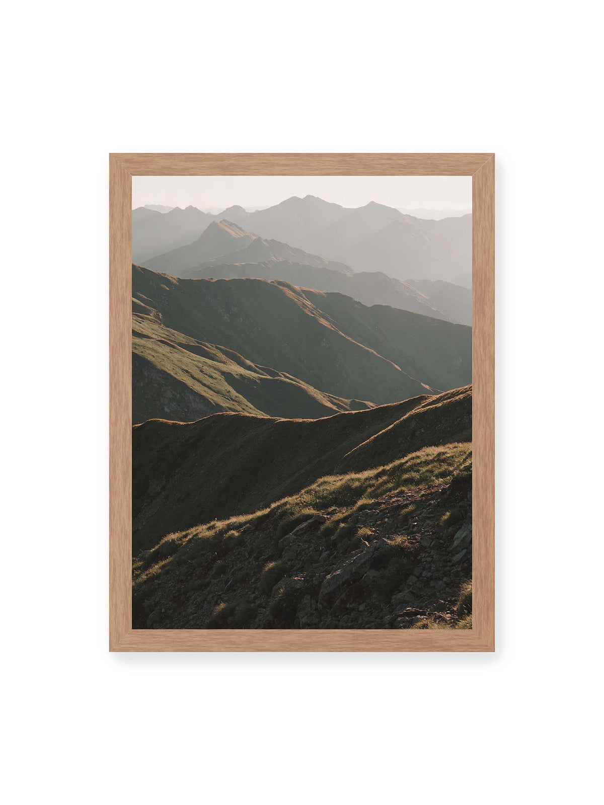 30x40 cm, Eichenrahmen – Gestaffelte Bergketten mit grasbewachsenen Hängen und warm beleuchteten Konturen unter hellem Himmel.