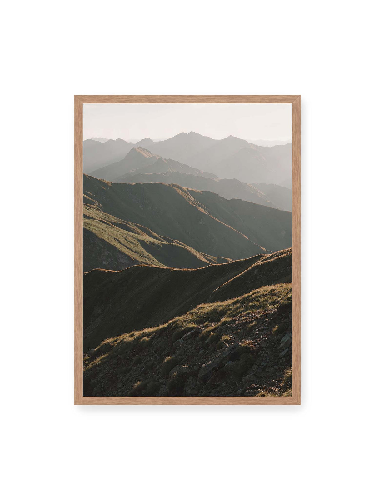 50x70 cm, Eichenrahmen – Gestaffelte Bergketten mit grasbewachsenen Hängen und warm beleuchteten Konturen unter hellem Himmel.