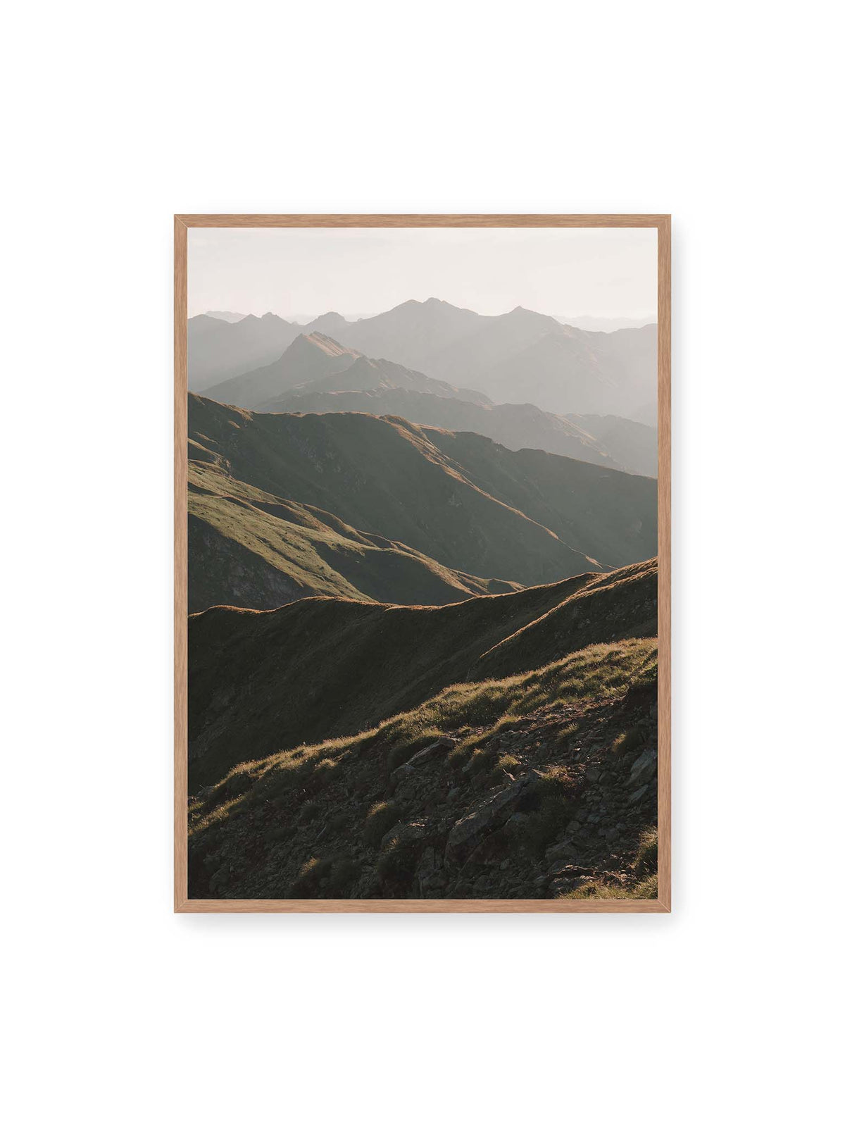 70x100 cm, Eichenrahmen – Gestaffelte Bergketten mit grasbewachsenen Hängen und warm beleuchteten Konturen unter hellem Himmel.