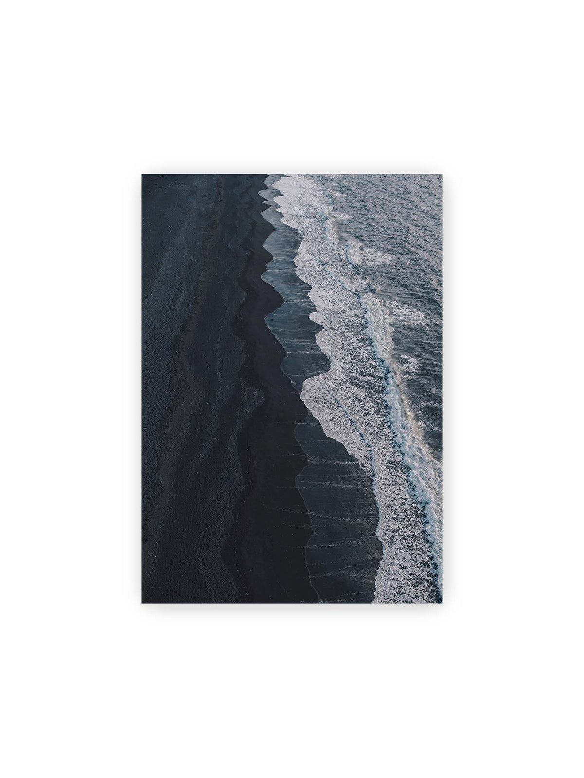 21x30 cm – Dunkler Strand aus erhöhter Perspektive mit weißer Brandung und blau-grauem Meer entlang einer geschwungenen Küstenlinie.