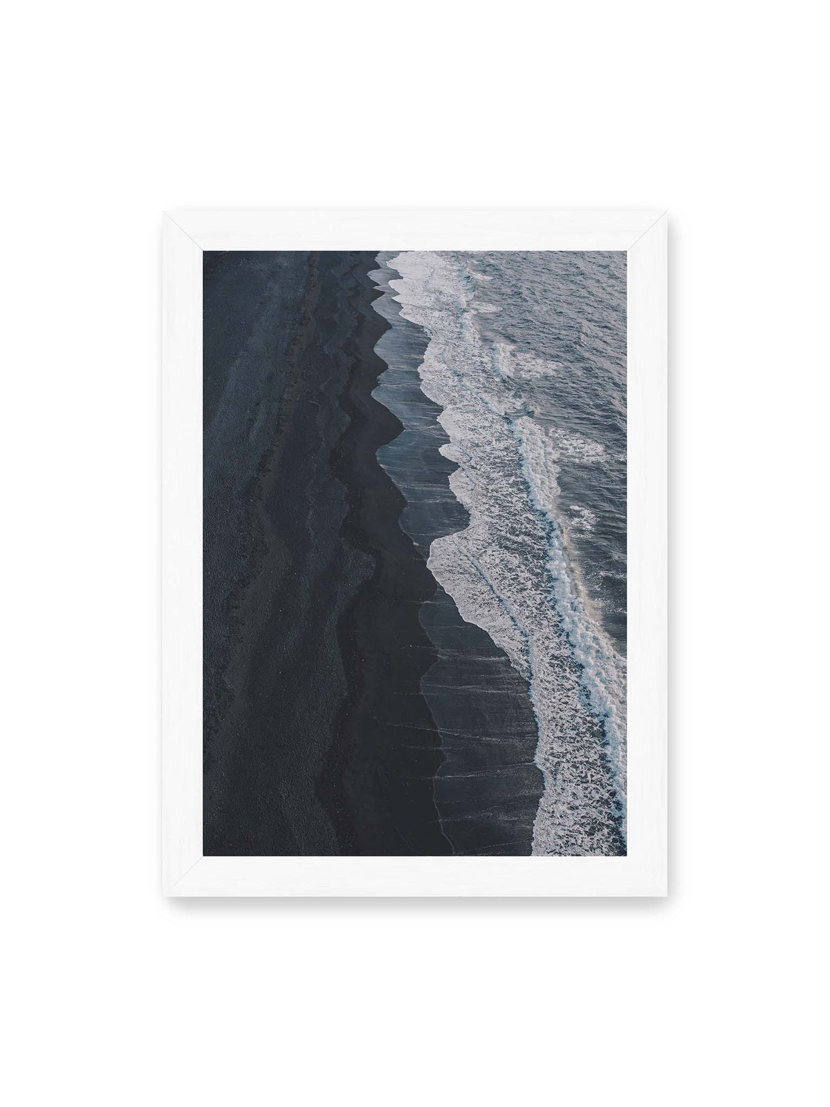 21x30 cm, weißer Rahmen – Dunkler Strand aus erhöhter Perspektive mit weißer Brandung und blau-grauem Meer entlang einer geschwungenen Küstenlinie.
