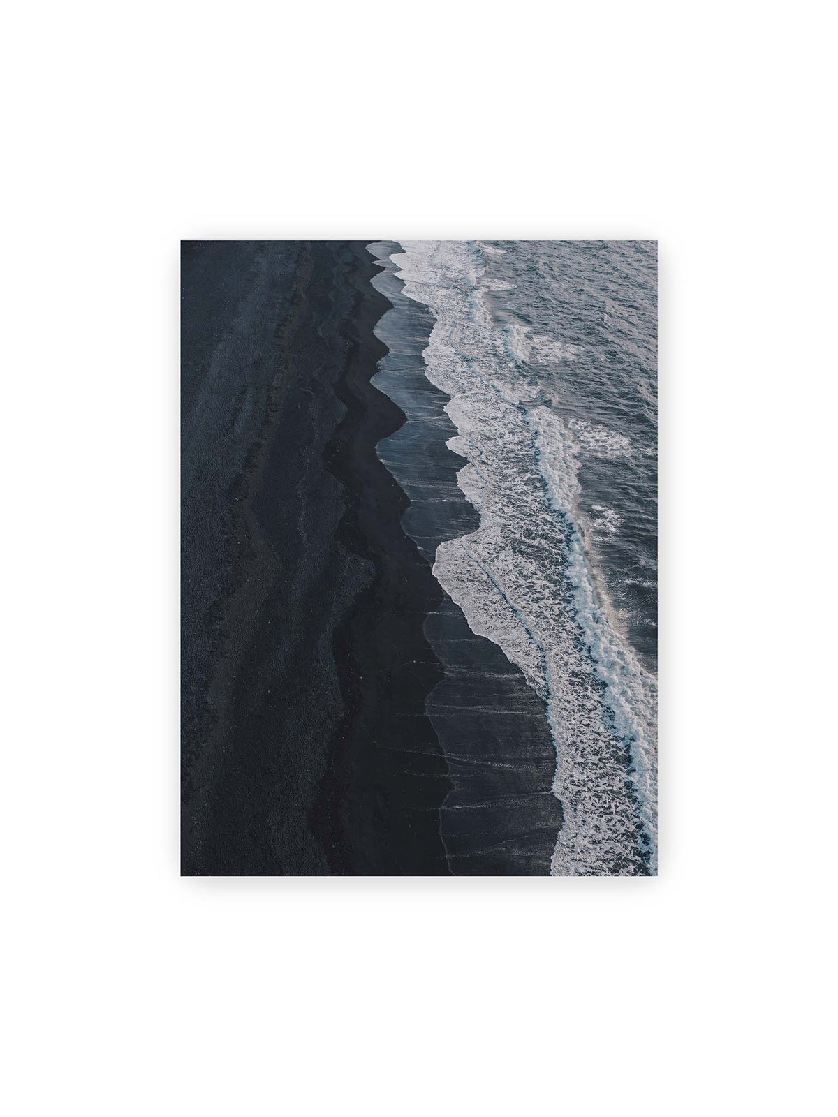 30x40 cm – Dunkler Strand aus erhöhter Perspektive mit weißer Brandung und blau-grauem Meer entlang einer geschwungenen Küstenlinie.